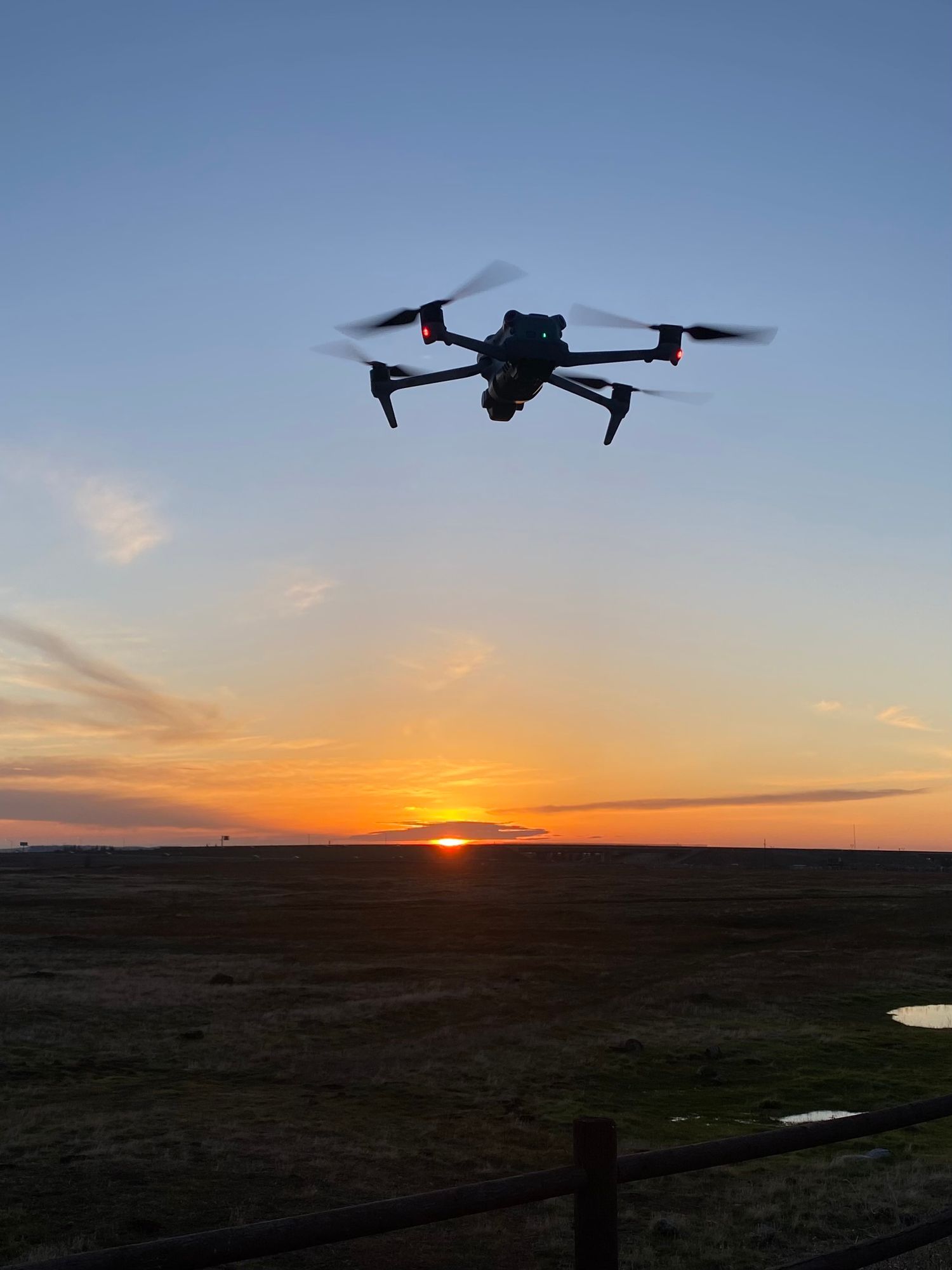 A drone hovers in the sky capturing a dramatic sunset over a vast open landscape with golden hues on the horizon.