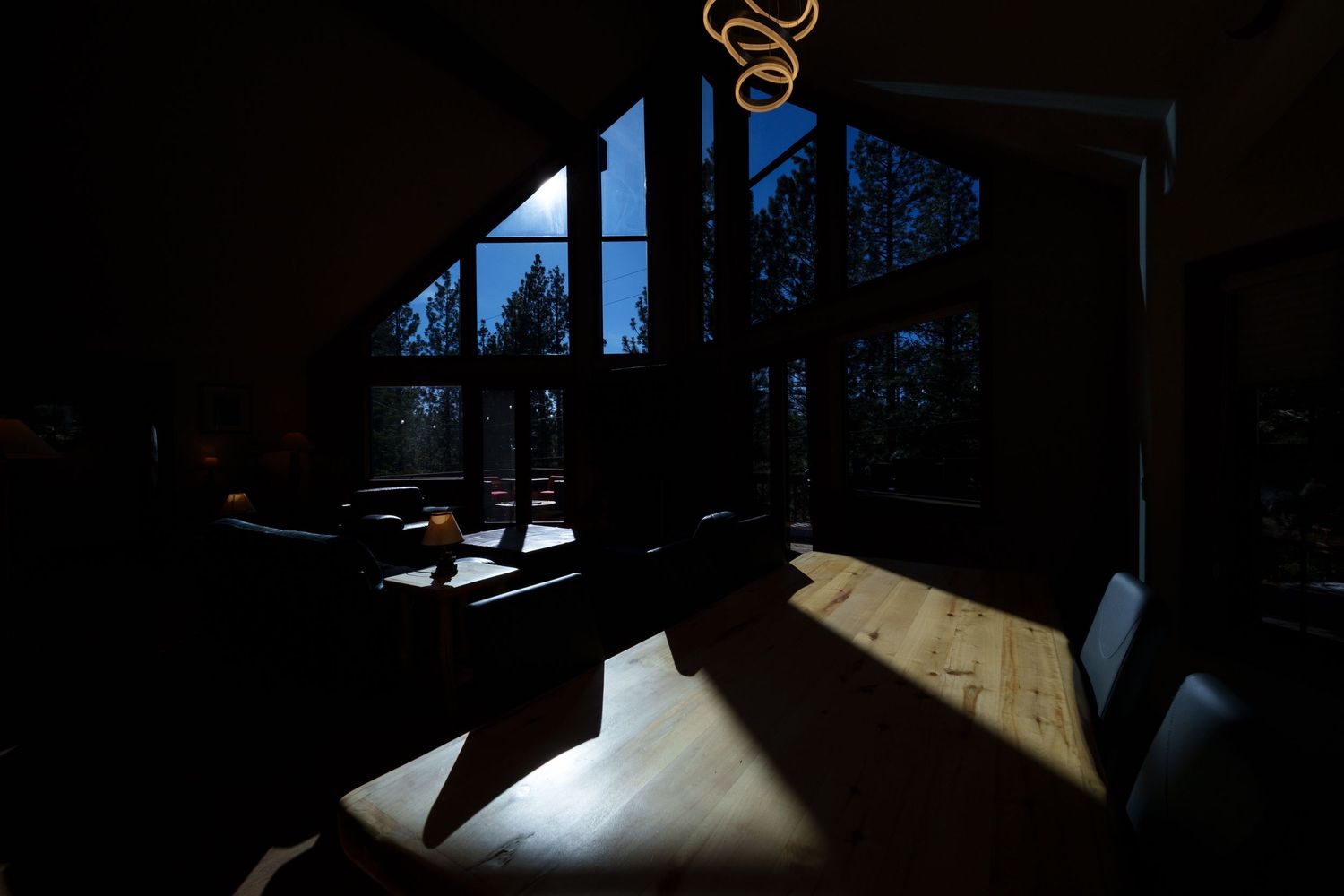 Dramatic silhouette of dining furniture against large windows with mountain views at sunset.