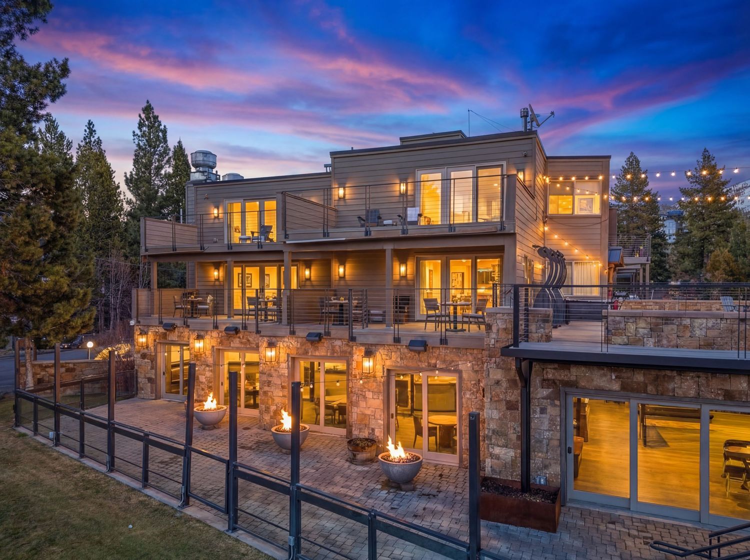 Modern luxury mountain home exterior with warm lighting and stone accents captured at dusk in panoramic view.