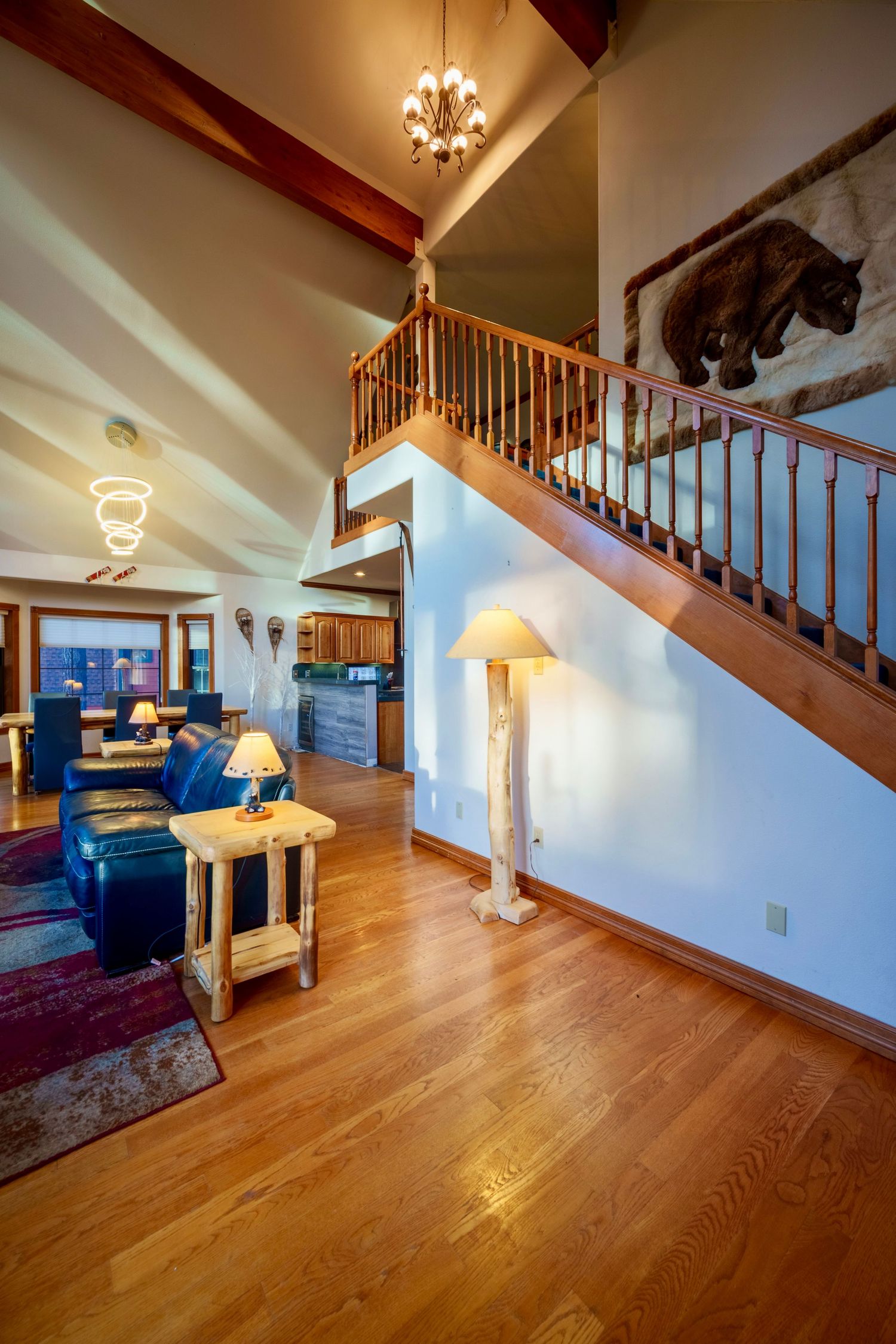 Interior view of open concept living area with hardwood floors, staircase, and warm lighting from chandelier.