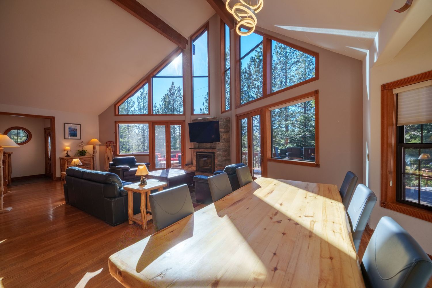 Open concept living space with tall windows, wood dining table, and grey sofa in sunlit room.