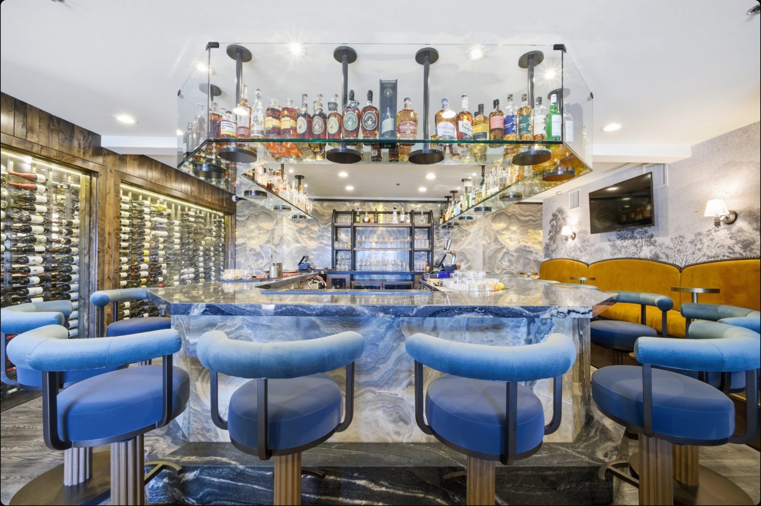 Elegant bar with blue marble countertop, blue bar stools, and shelves of liquor bottles with pendant lighting.