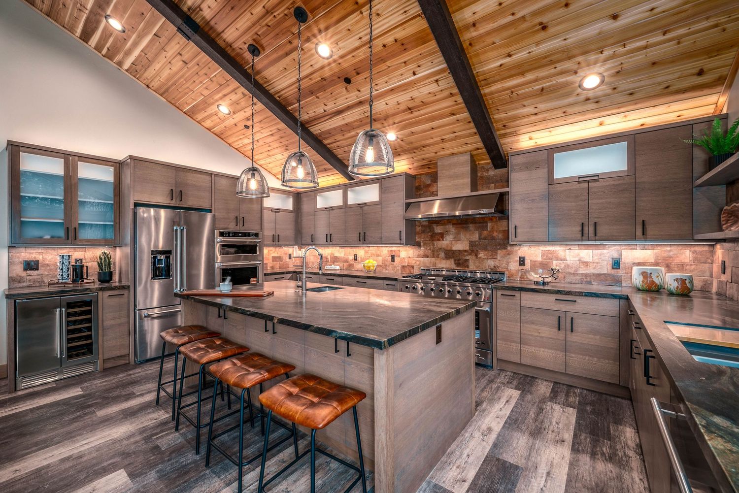 Modern rustic kitchen with vaulted wood ceiling, pendant lights, large island with bar seating, and stainless steel appliances.