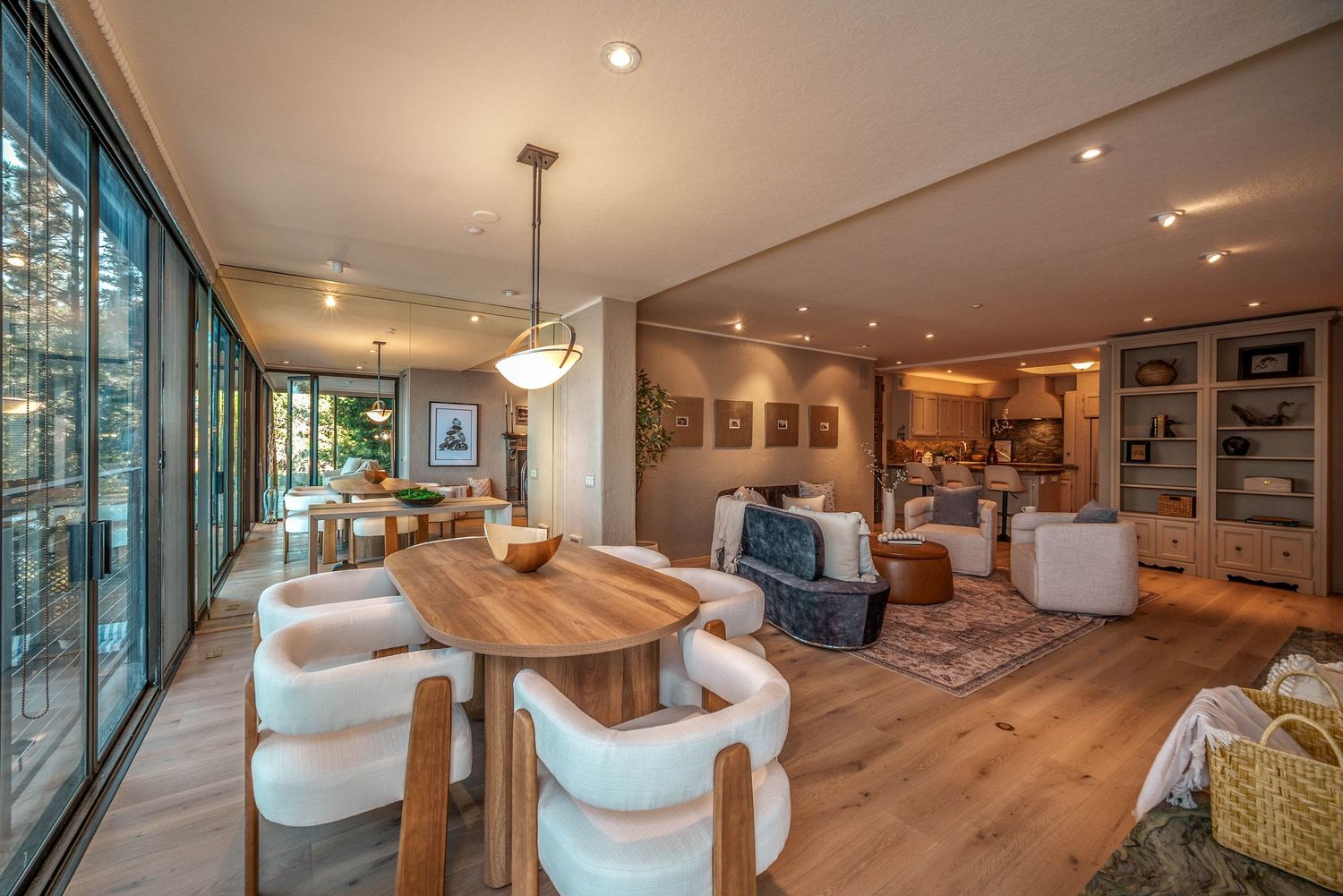 Spacious open-concept living and dining area with a wood table, cream chairs, hardwood floors, built-in shelving, and floor-to-ceiling windo