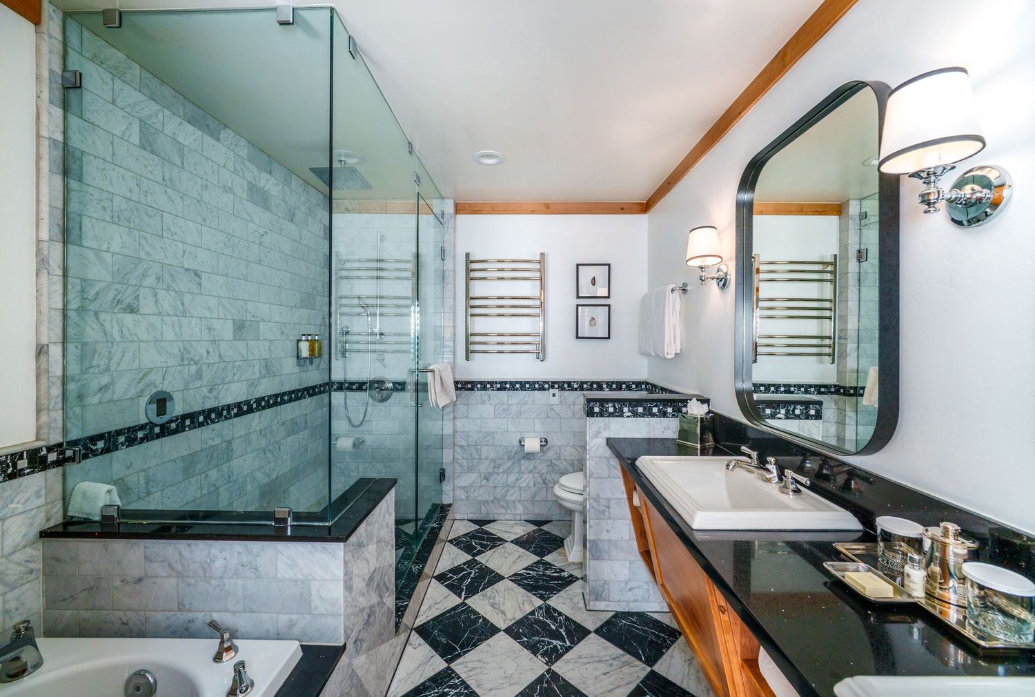 Modern bathroom features black and white checkered floor tiles, glass shower enclosure, and warm wood accents.