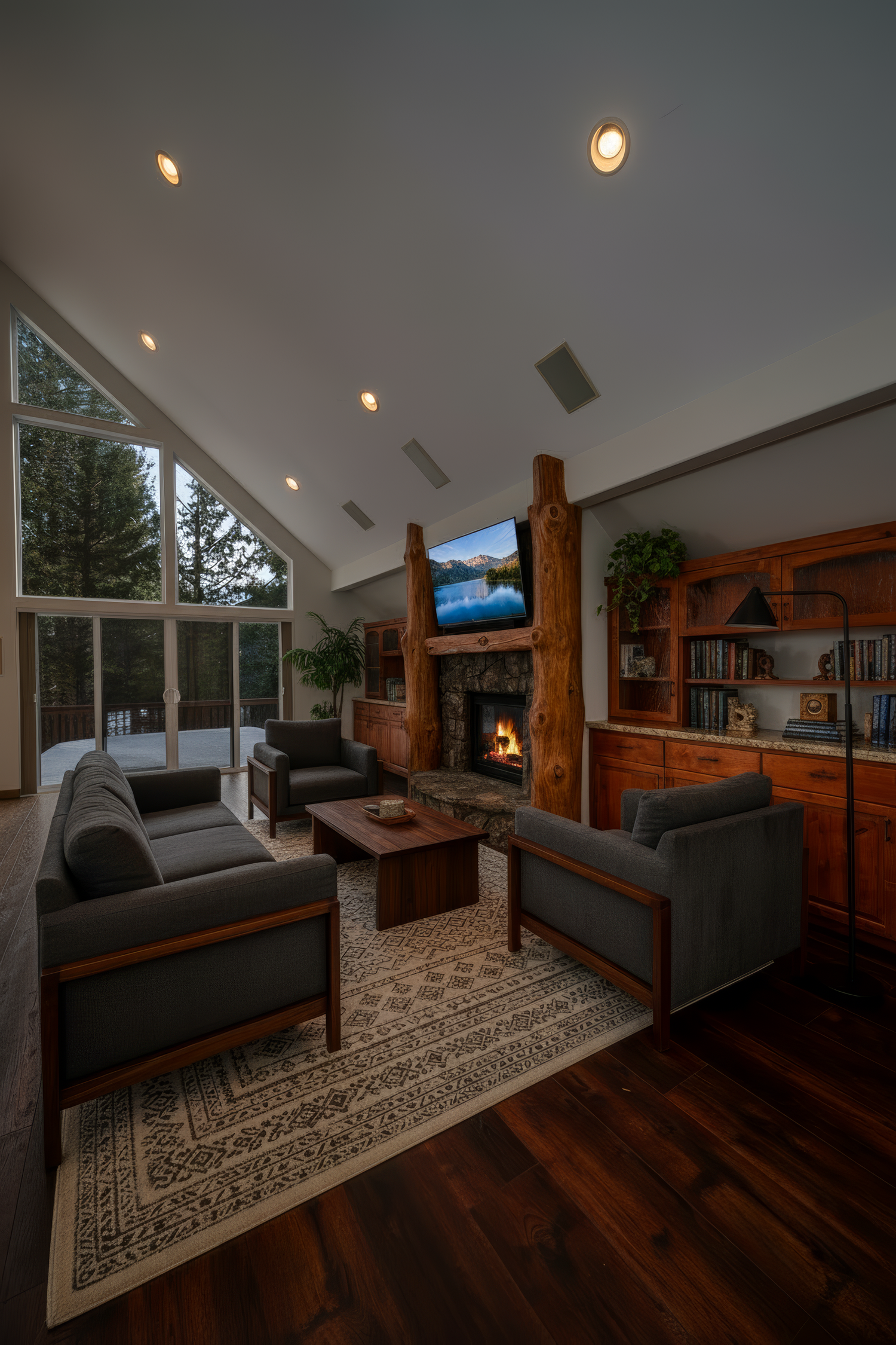 Modern mountain home living room with vaulted ceiling, rustic wood accents, stone fireplace and dark hardwood floors.
