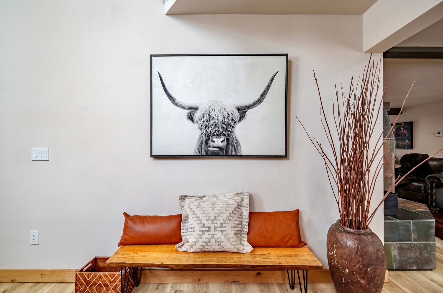 Modern rustic living room features longhorn skull decor, orange accent pillows, and natural wood furniture.