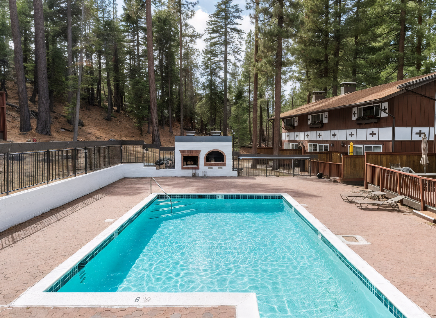 A pristine turquoise swimming pool surrounded by tall pine trees at a mountain resort property.