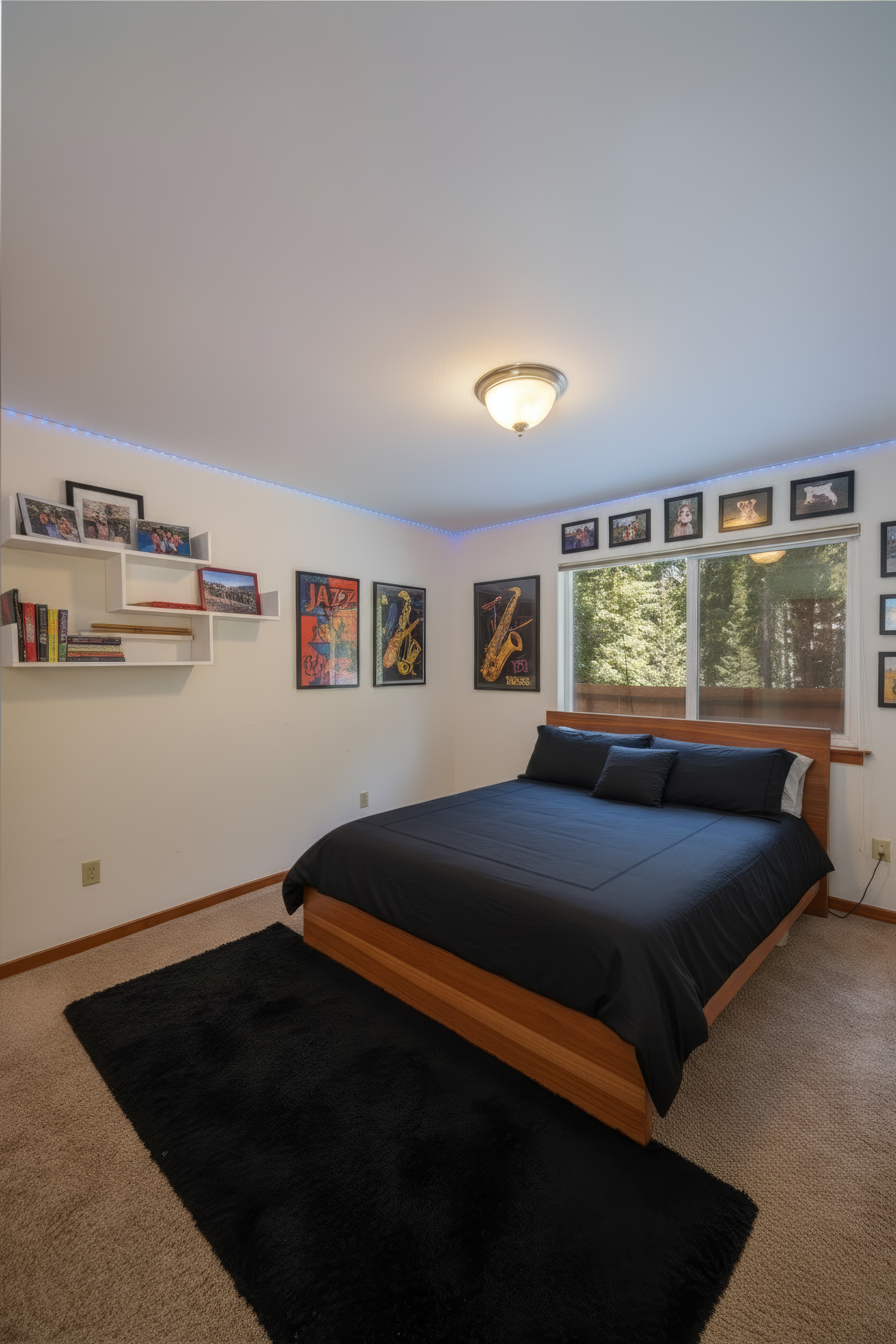 Cozy loft bedroom with black bedding, carpeted floors, and framed photos displayed along white walls in natural lighting.