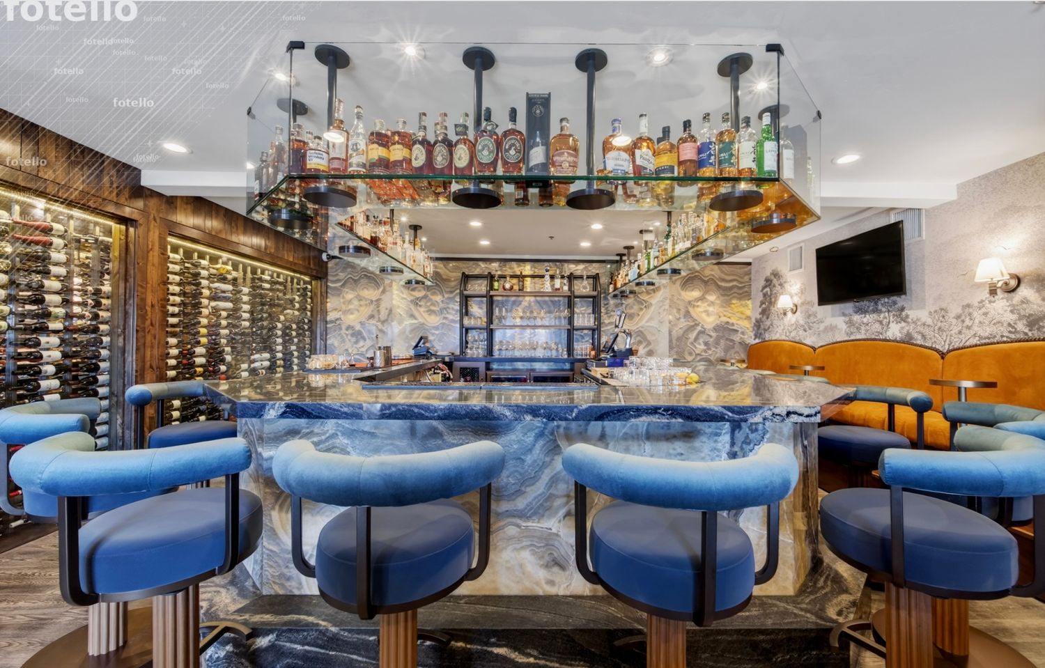 Elegant bar with blue velvet stools, glowing onyx countertop, and shelves of spirits beneath pendant lights.
