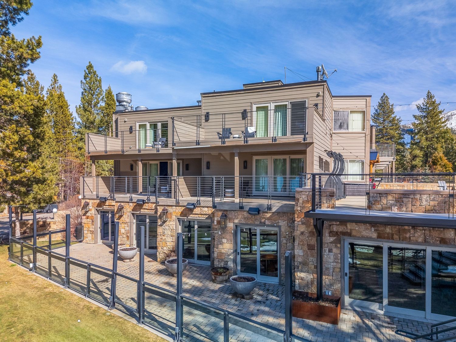 Modern hillside home with multiple levels featuring glass railings and contemporary architecture against a blue sky.