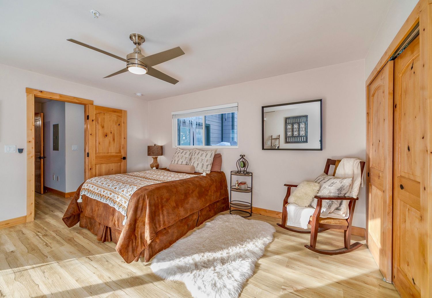 Modern farmhouse bedroom features light wood trim, white walls, and a ceiling fan in a bright, airy space.
