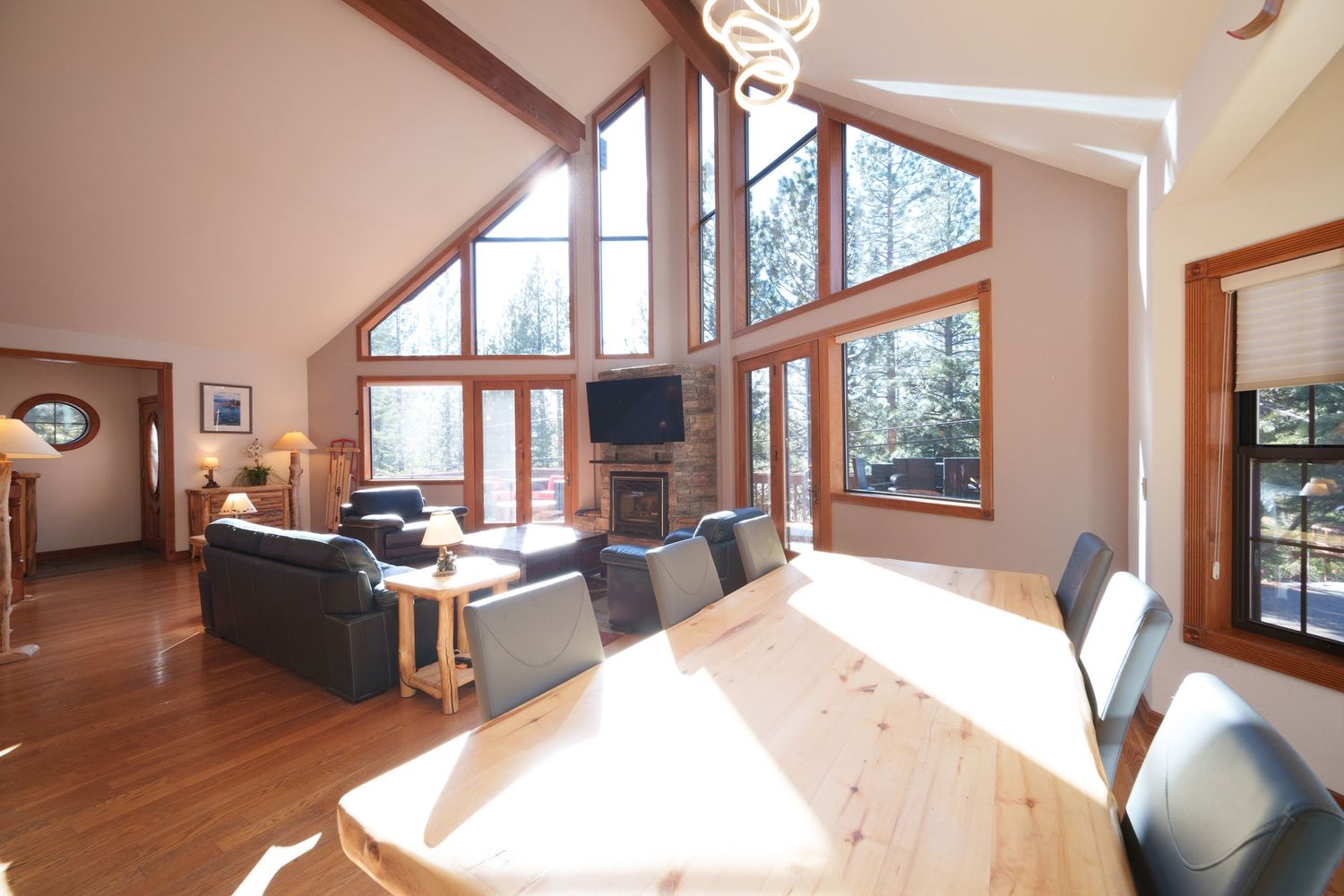 Modern mountain home living room with vaulted ceiling, large windows, and natural light streaming onto dining table.
