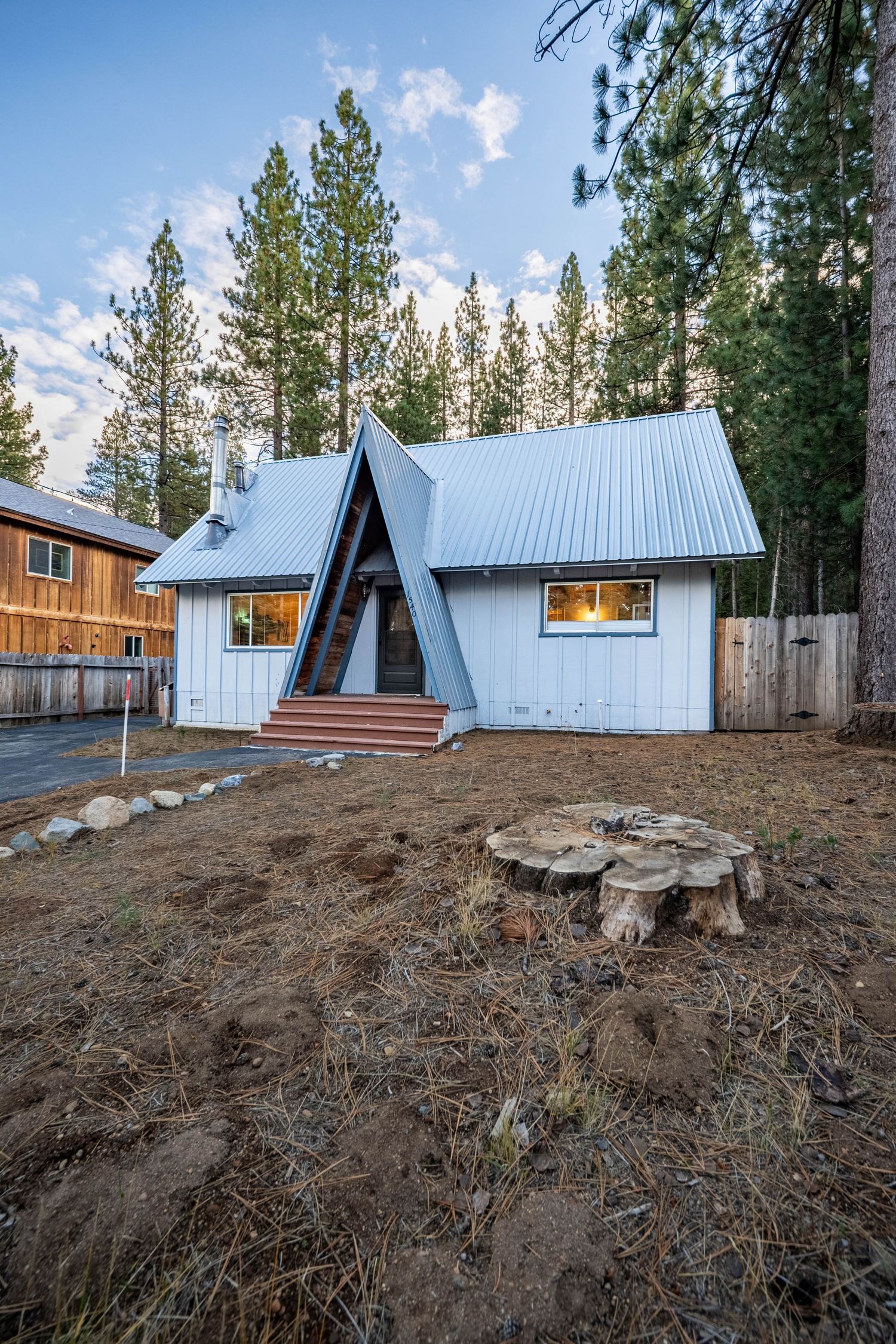 Modern A-frame style house with blue metal roof surrounded by pine trees.