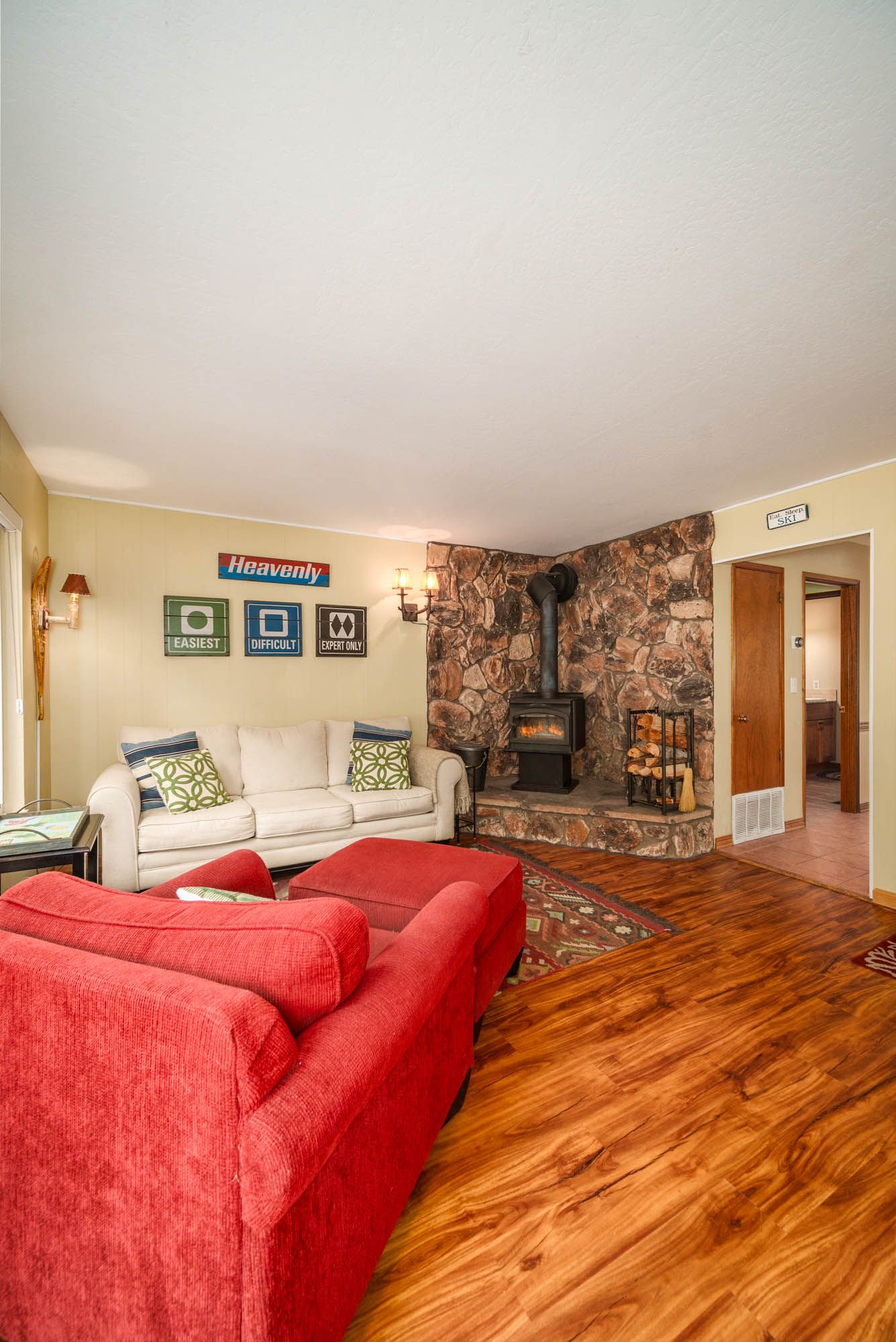 Cozy living room with red sofas, a white couch, a stone fireplace with wood stove, and warm hardwood floors.