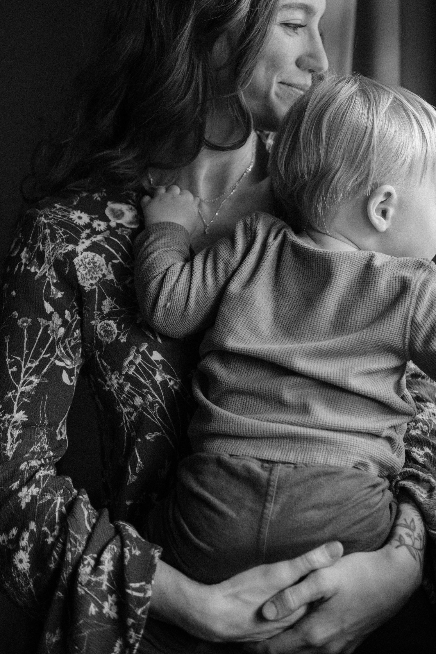 Black and white photo of a smiling mother tenderly holding her young toddler child in a warm embrace.