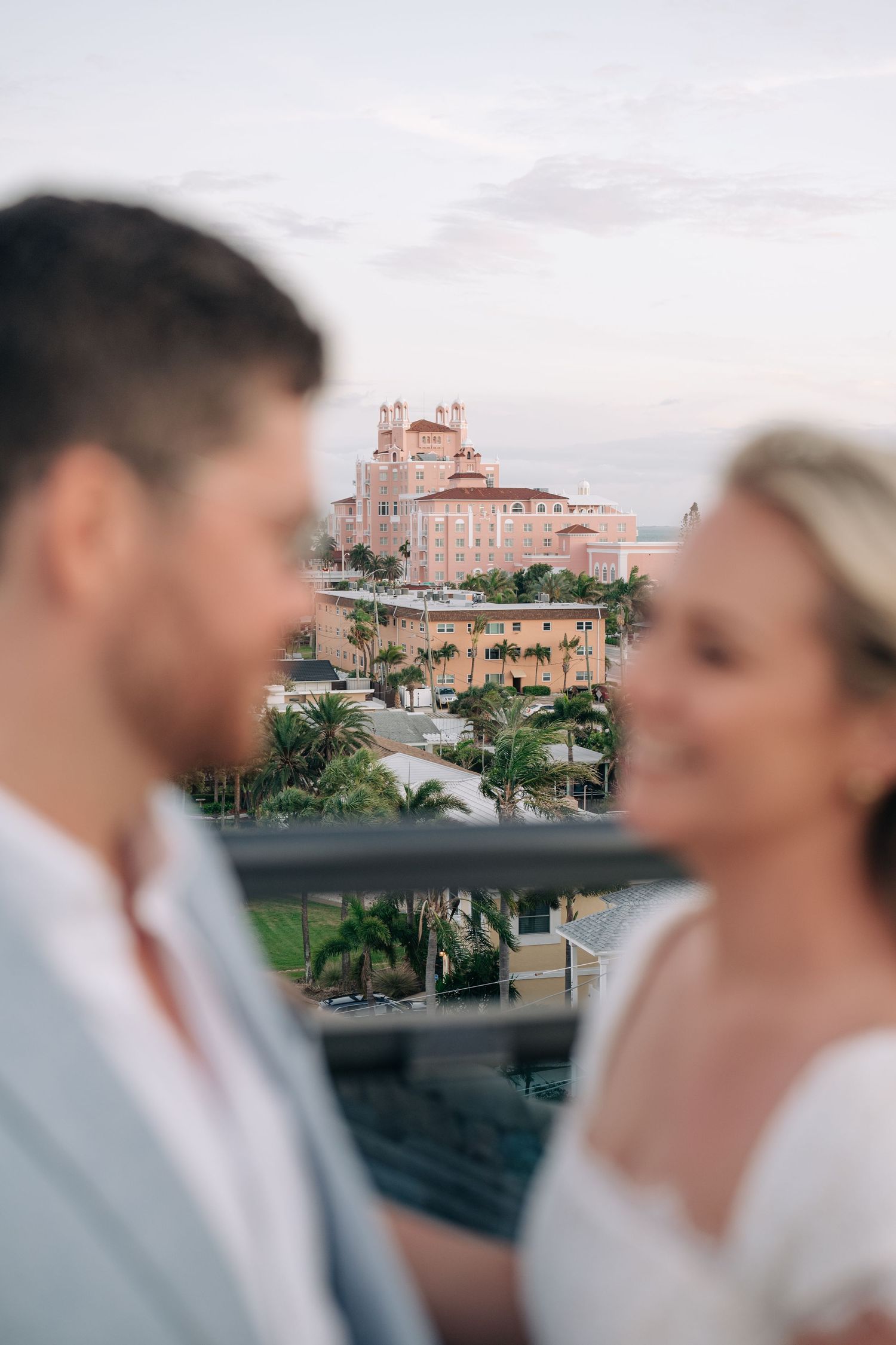 Couple shares romantic moment on balcony with iconic pink Don CeSar hotel in St. Pete Beach background.