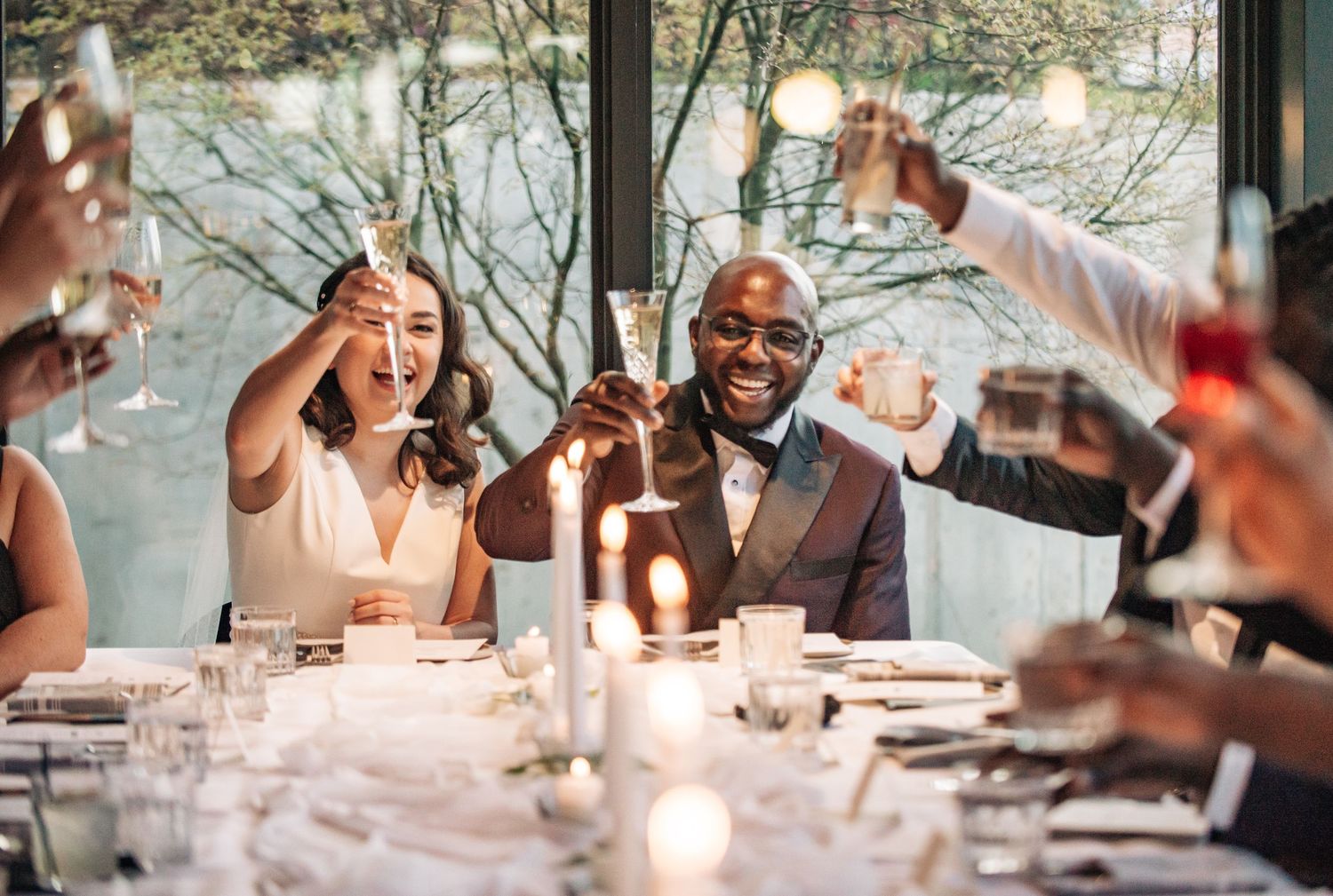 Bride and groom raising champagne glasses with guests at elegant wedding reception dinner table.