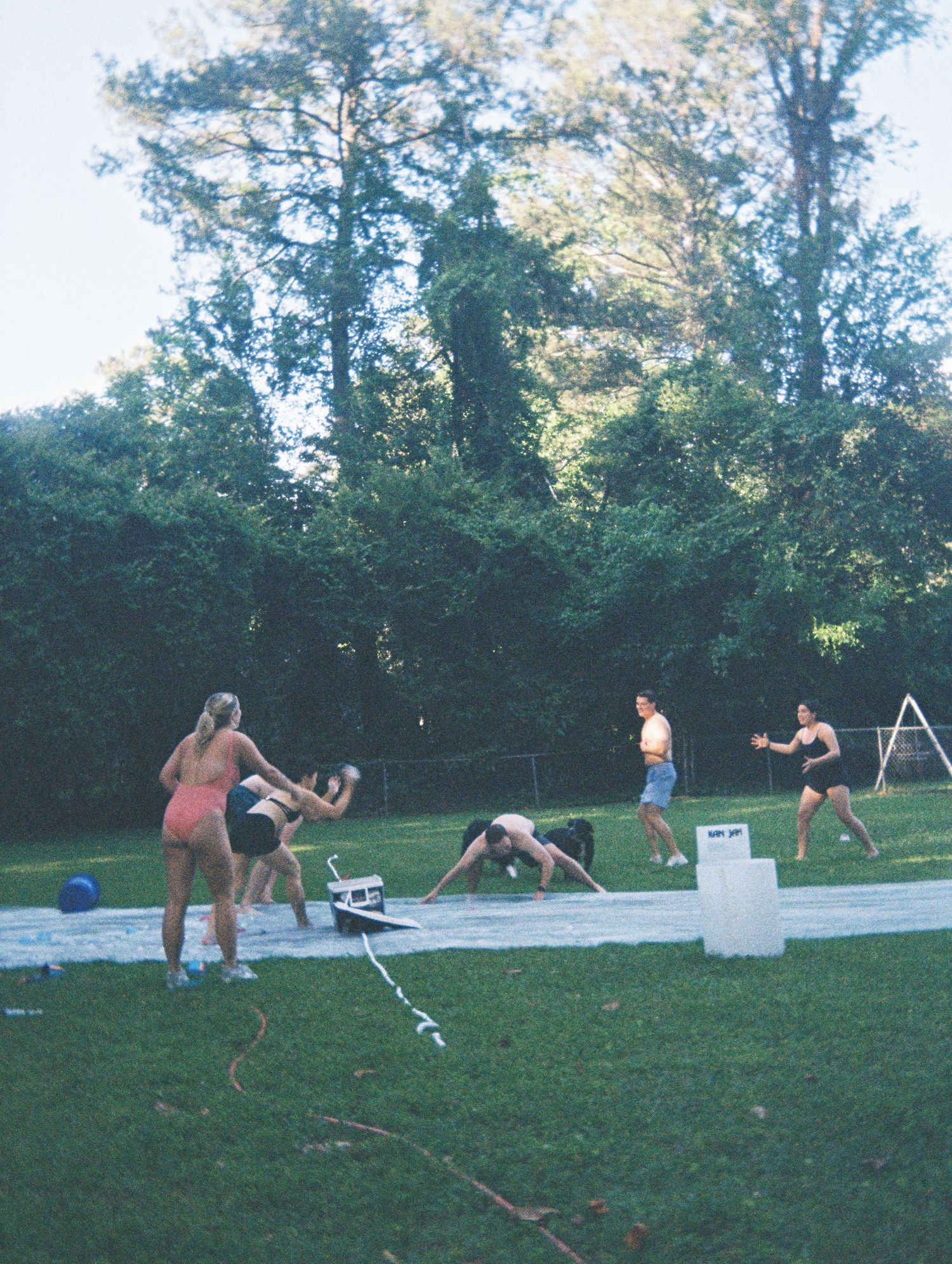 Group of friends playing on a backyard slip-and-slide on a warm summer evening.