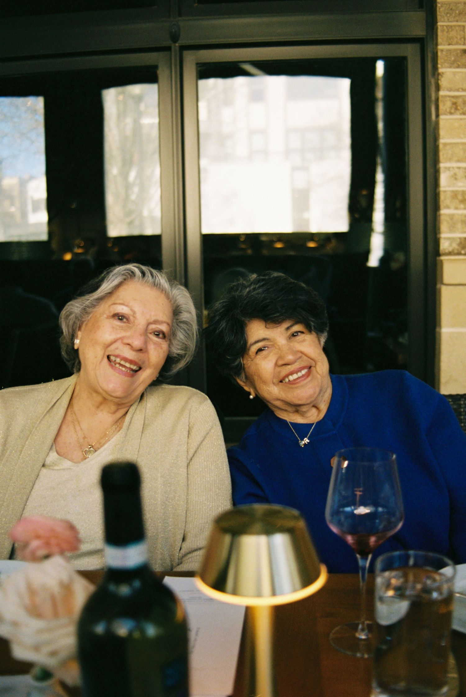Two smiling grandmas dining at restaurant table with wine glasses and candle at an intimate wedding.