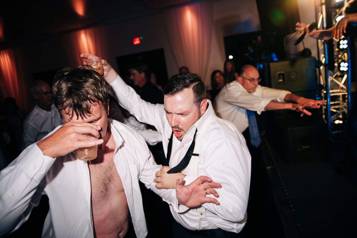 Men in white dress shirts dancing energetically at a wedding reception party.