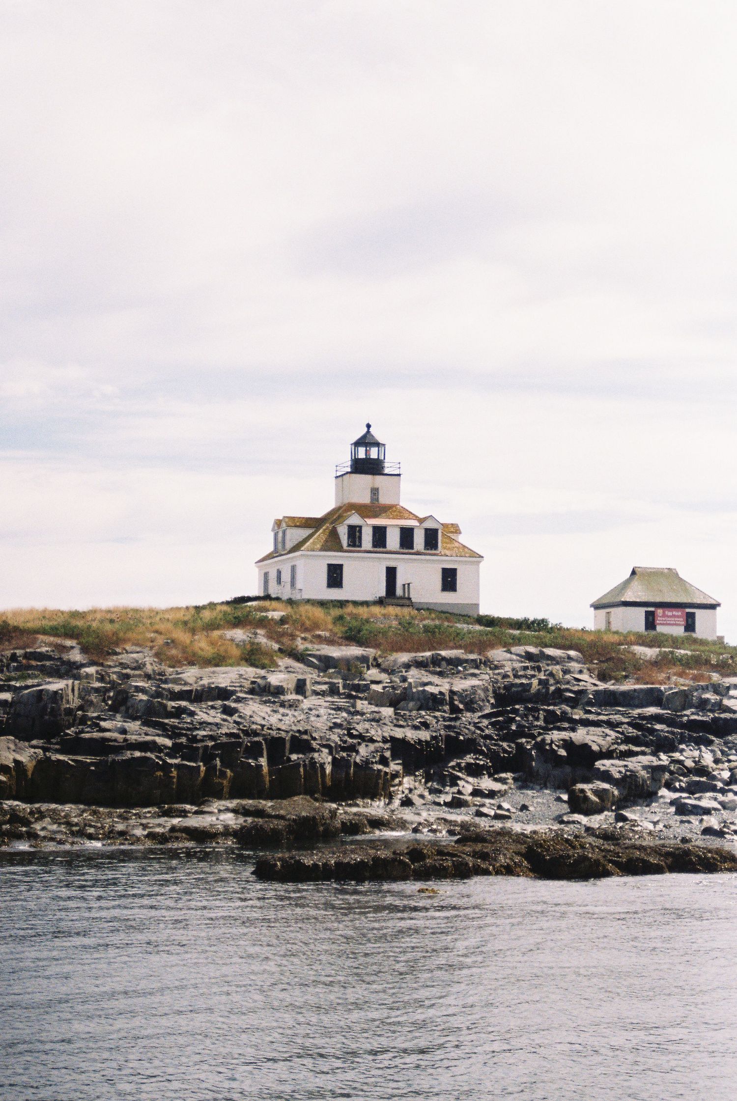 White lighthouse with yellow roof perched on rocky coastal island under overcast sky.