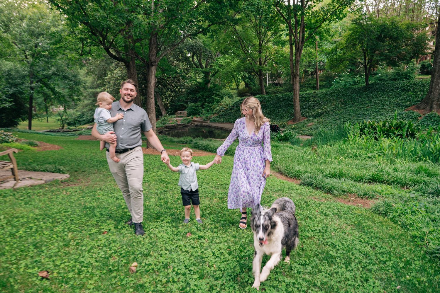 Family with two kids and a dog walking in a lush green park on a sunny day.