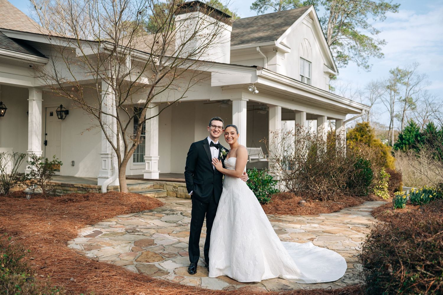 Bride and groom posing together in front of a white farmhouse wedding venue on a winter day.