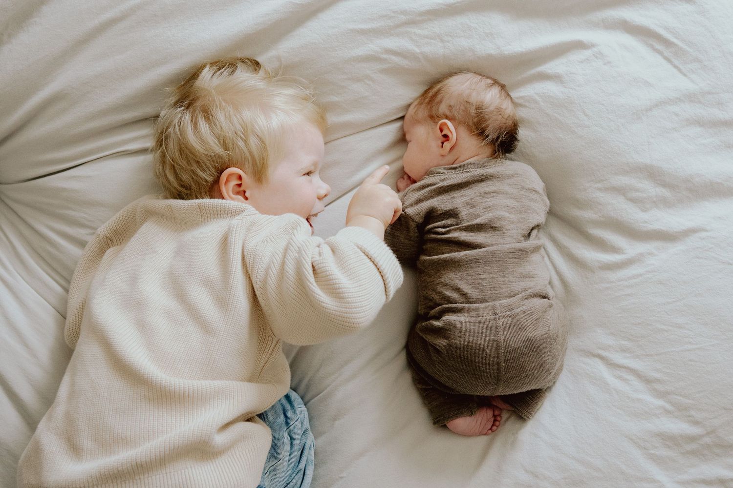 Geschwister liegen nebeneinander auf dem Bett, Newborn-Shooting