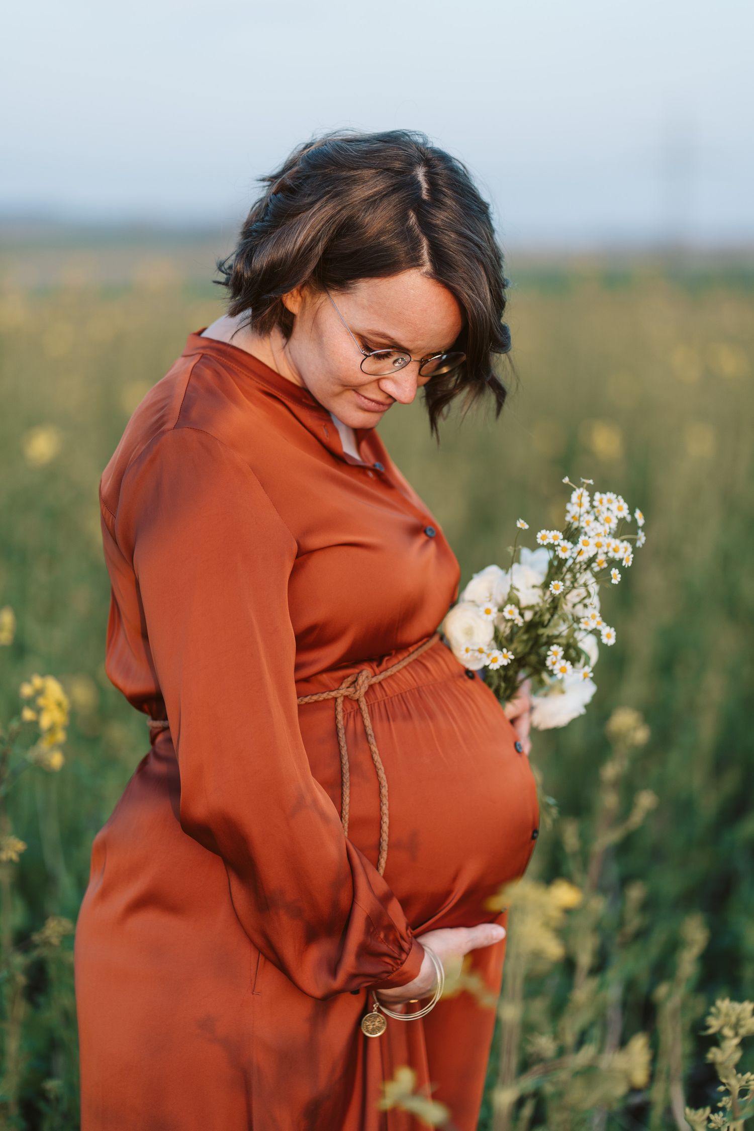 Schwangere im roten Kleid mit Blumen auf einem Feld, Babybauch-Shooting