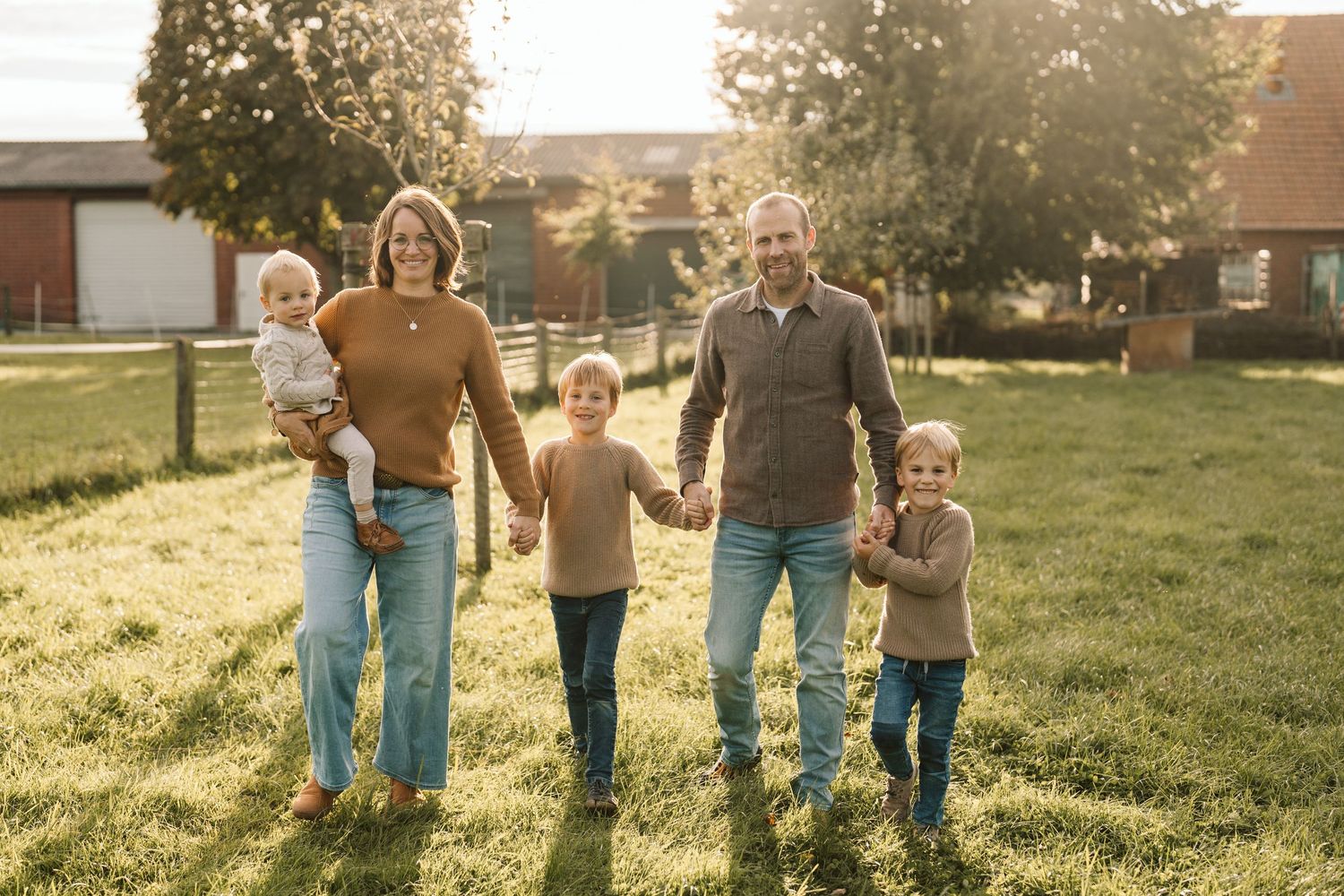 Familie geht Hand in Hand über eine Wiese vor einem Haus