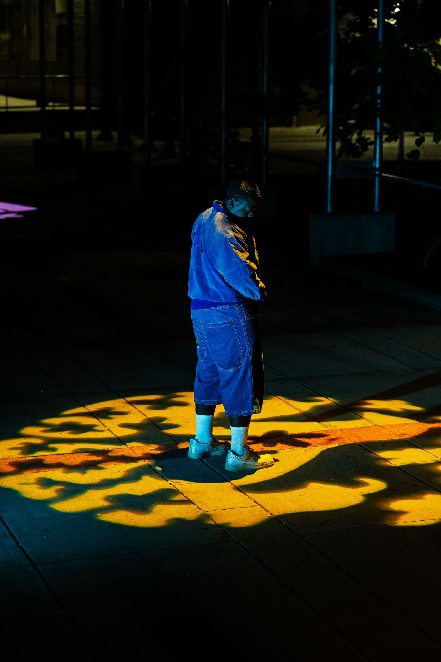 Person in blue outfit stands in yellow spotlight pattern cast on dark ground at night.