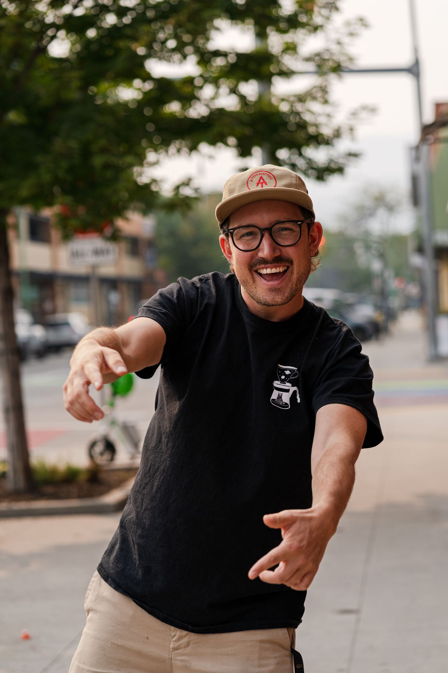 Person in black t-shirt and cap gesturing enthusiastically on urban street.