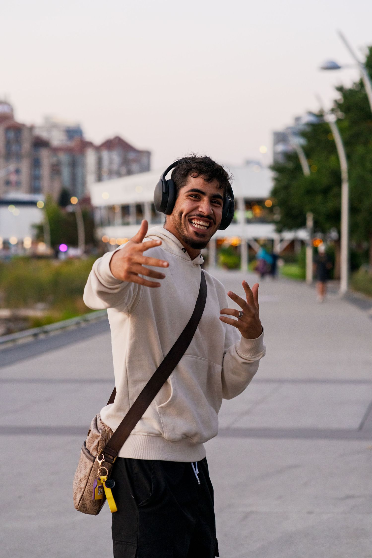 Person wearing headphones and white sweatshirt gestures enthusiastically on urban pathway.