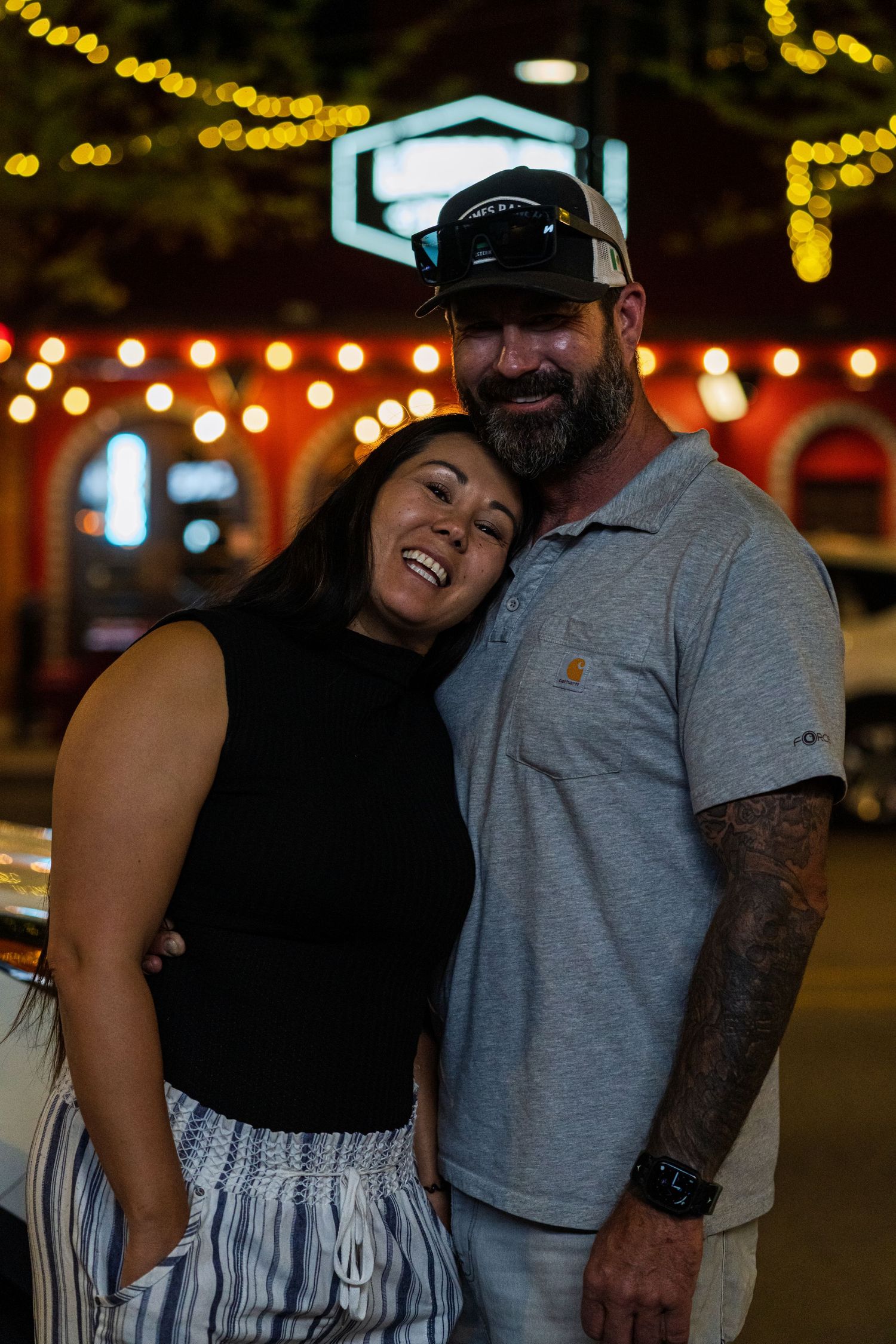 Happy couple sharing laughter under warm outdoor lighting and string lights.