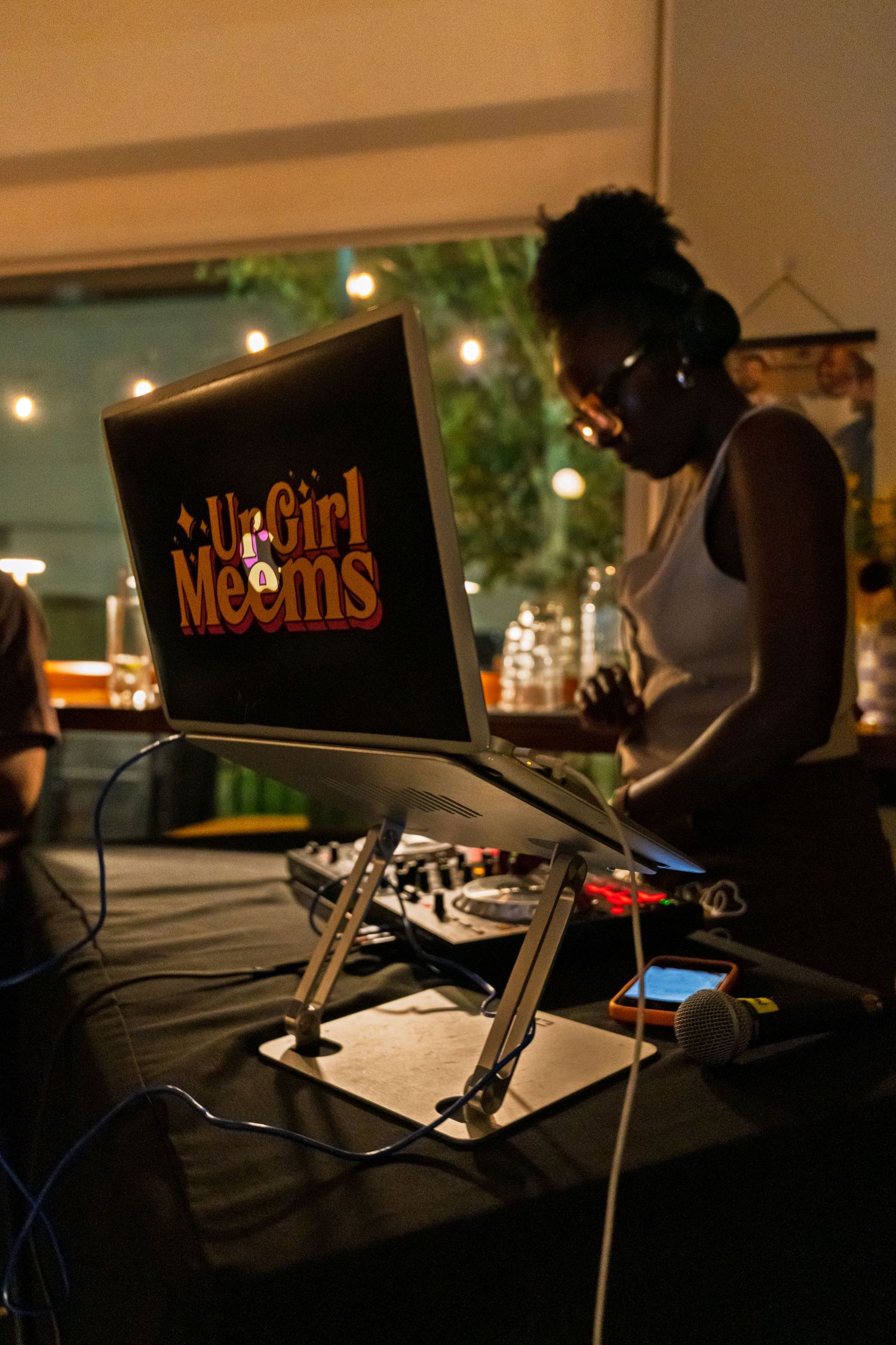 DJ performing at night event with laptop and equipment under warm string lights.