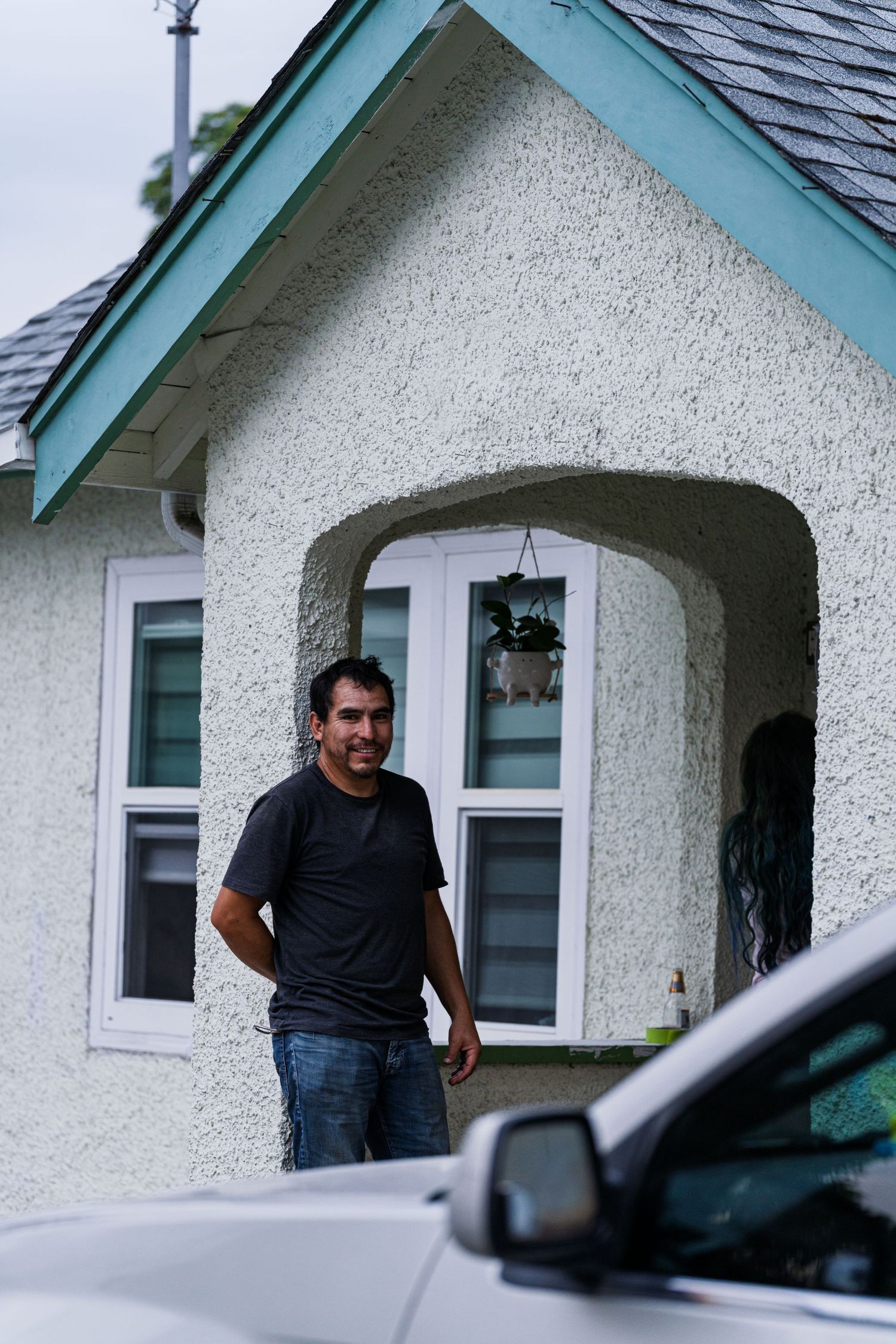 Person in a dark shirt stands in the doorway of a white stucco house with teal trim.