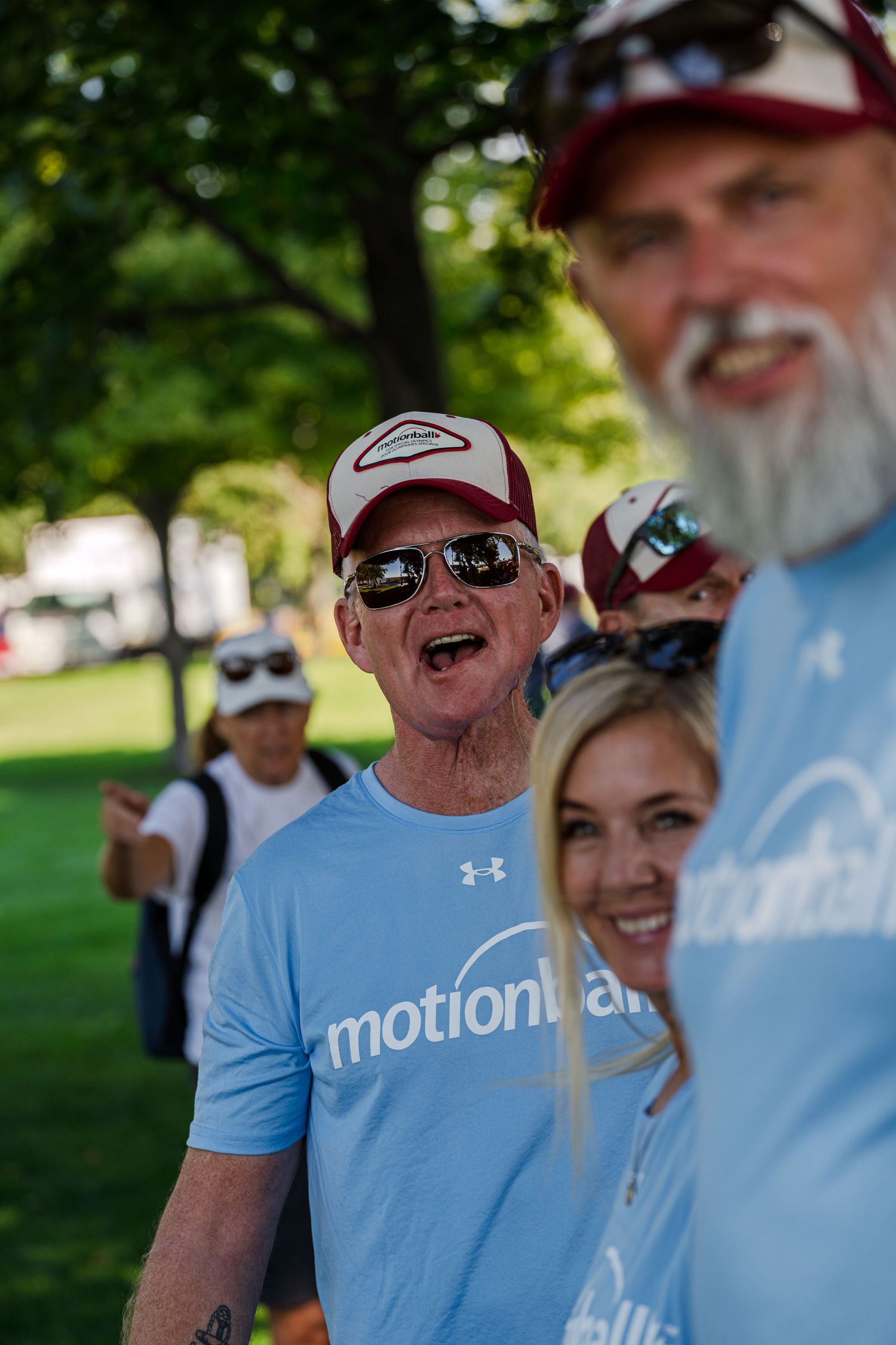 Group of people wearing light blue t-shirts and baseball caps enjoying an outdoor gathering in a park setting.