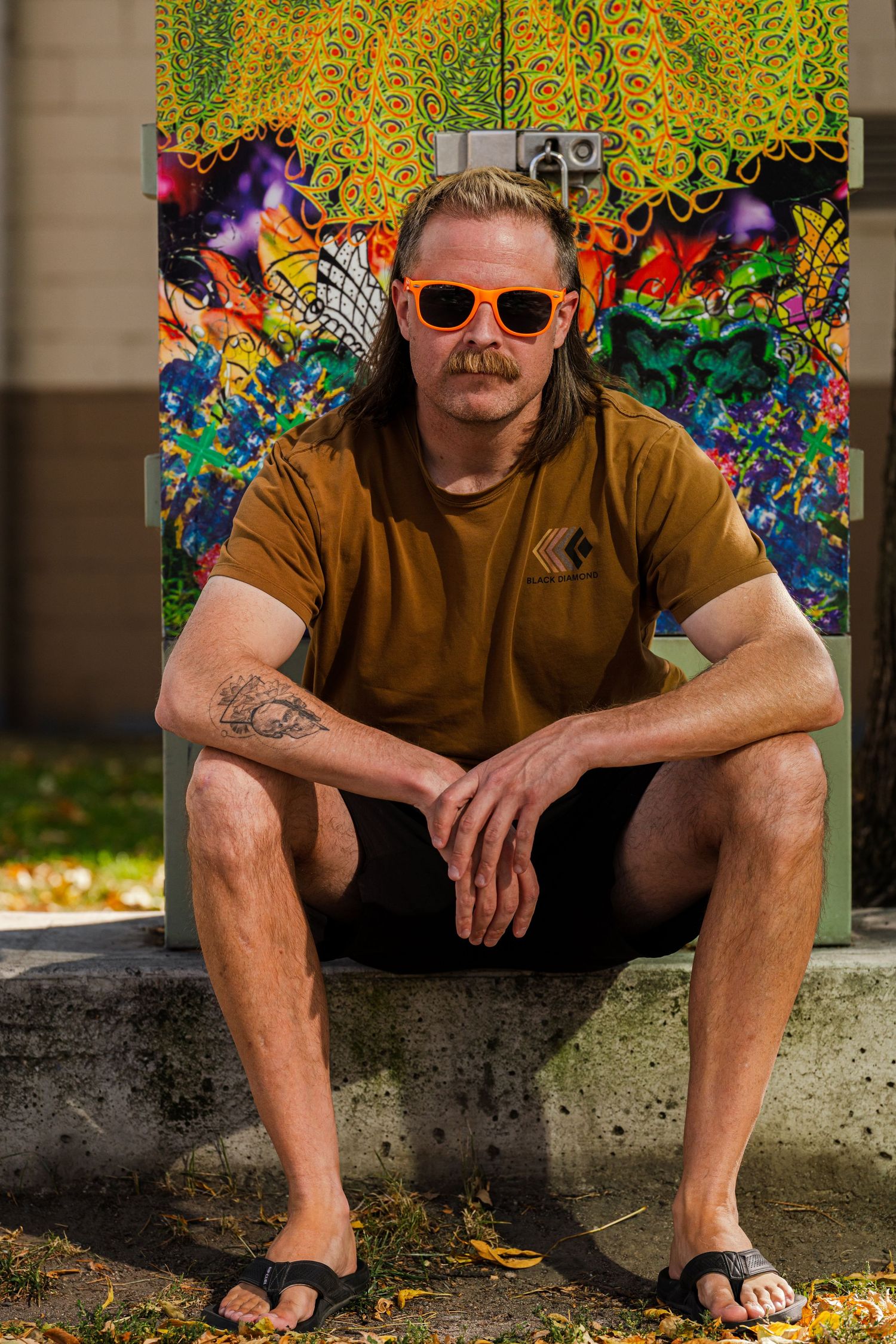 Person in brown shirt sitting on concrete ledge against colorful graffiti wall background.