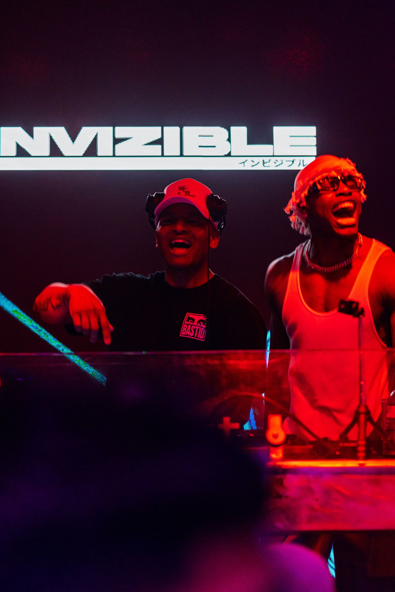 DJ performance setup with red lighting and 'NVIZIBLE' text display in dark nightclub setting.