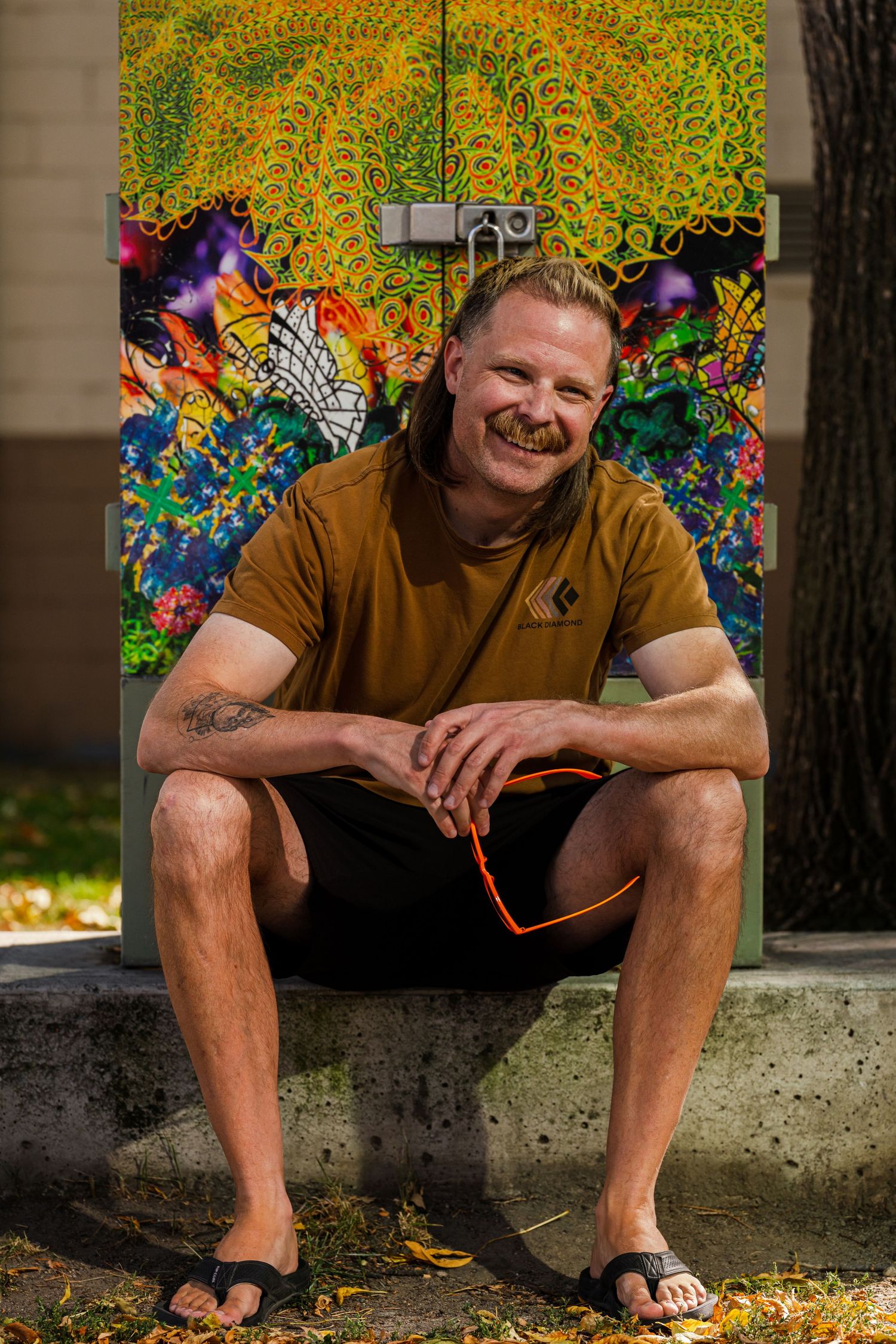 Person sits casually against colorful mural backdrop with sunflowers and butterflies.