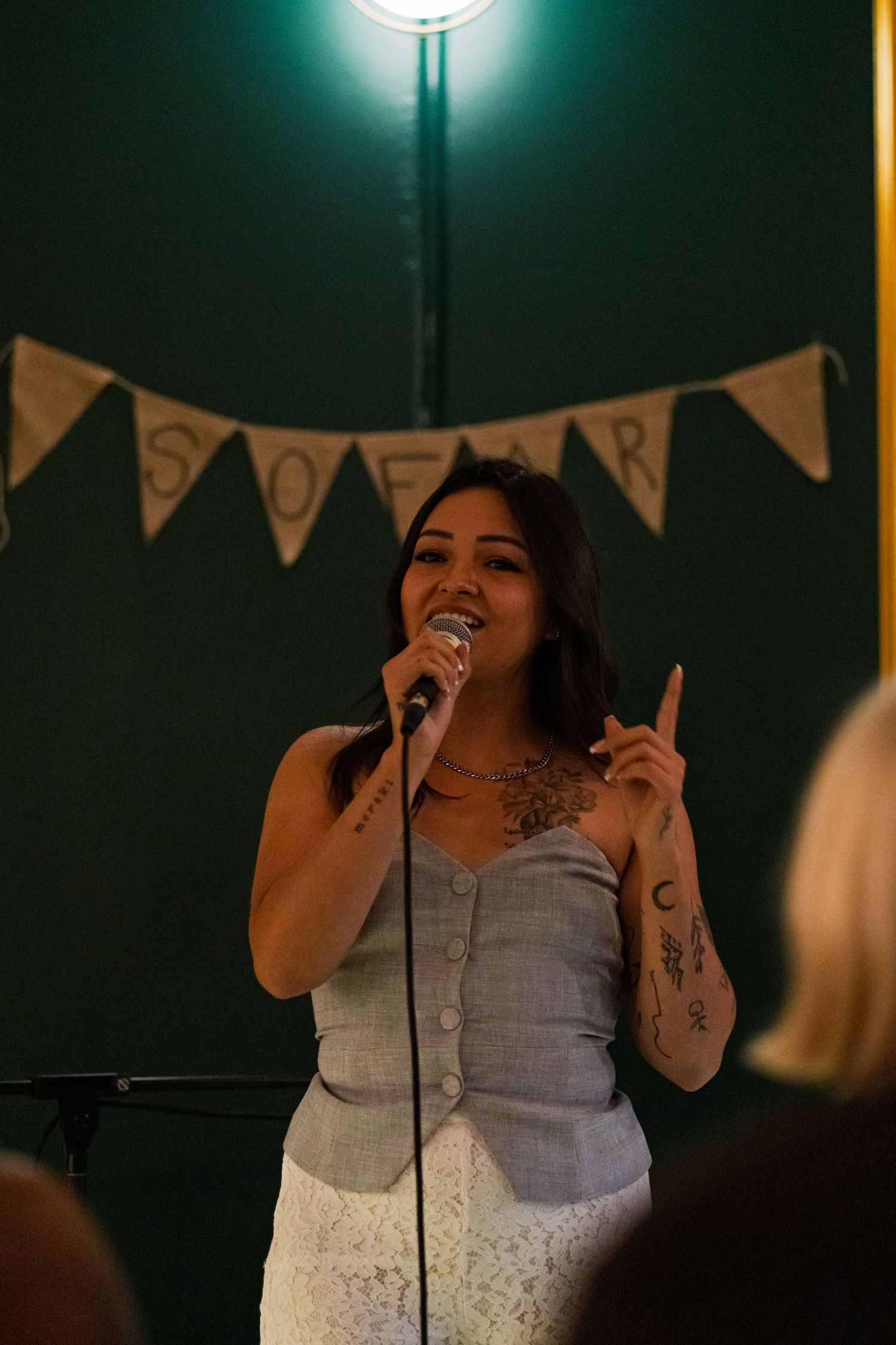 Performer singing on stage under green lighting with decorative banner in background.