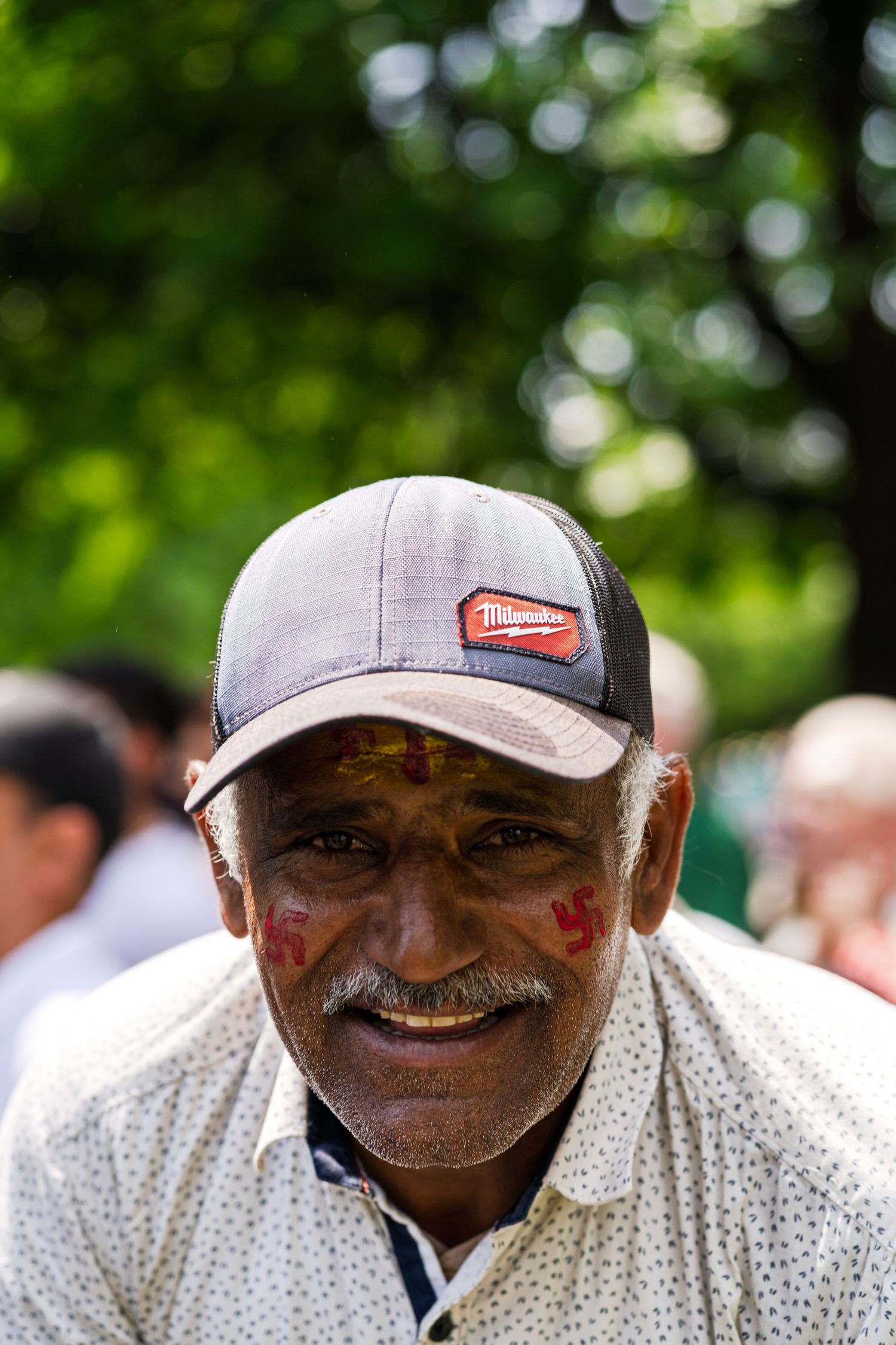 Person wearing baseball cap and polka dot shirt smiling outdoors in bright sunlight.