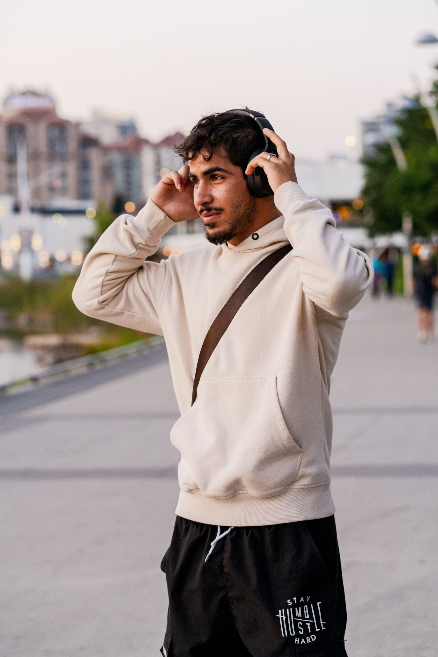 Person in cream hoodie and black shorts adjusting headphones while walking outdoors.