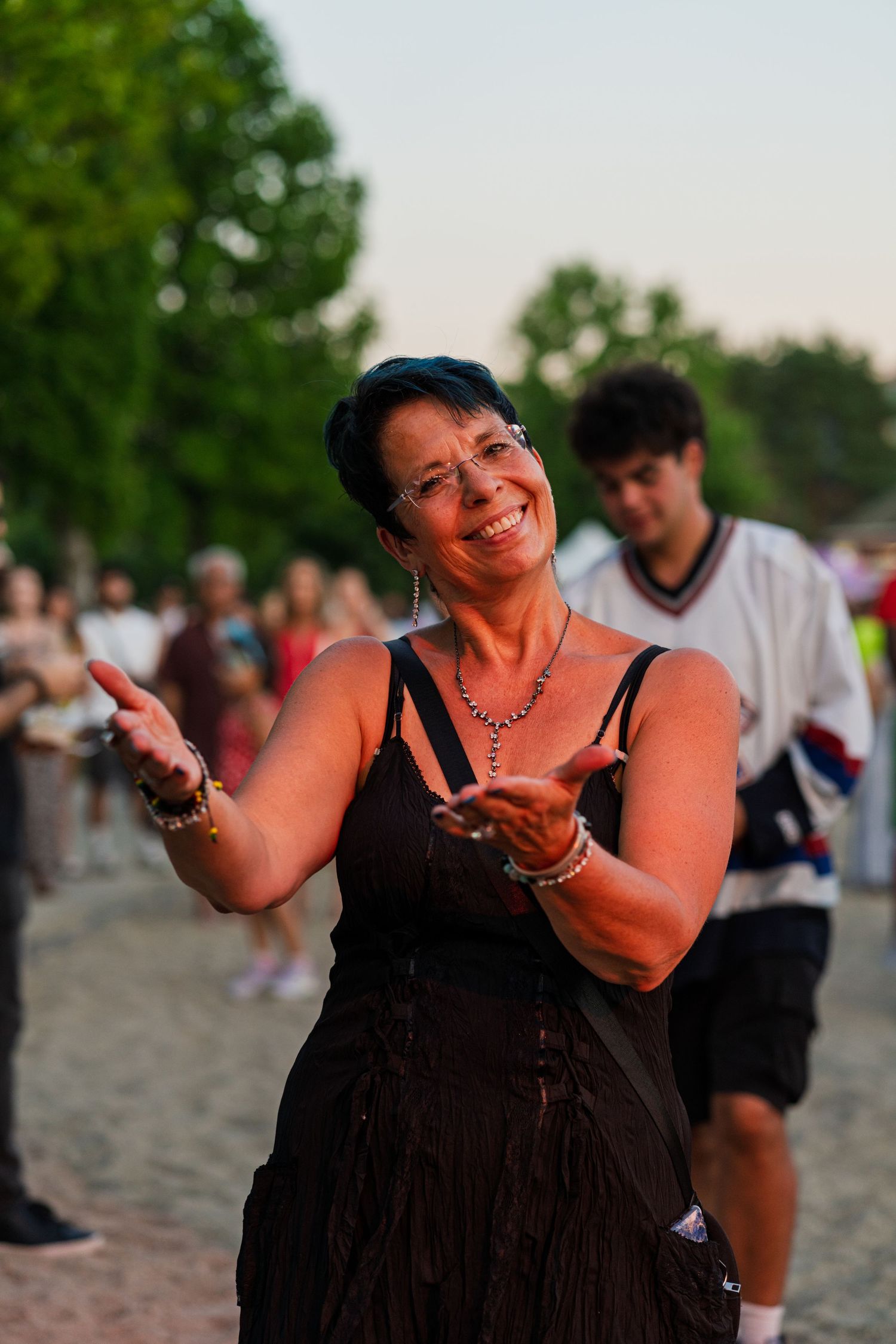 Person dancing joyfully on a beach at sunset with others visible in the background.