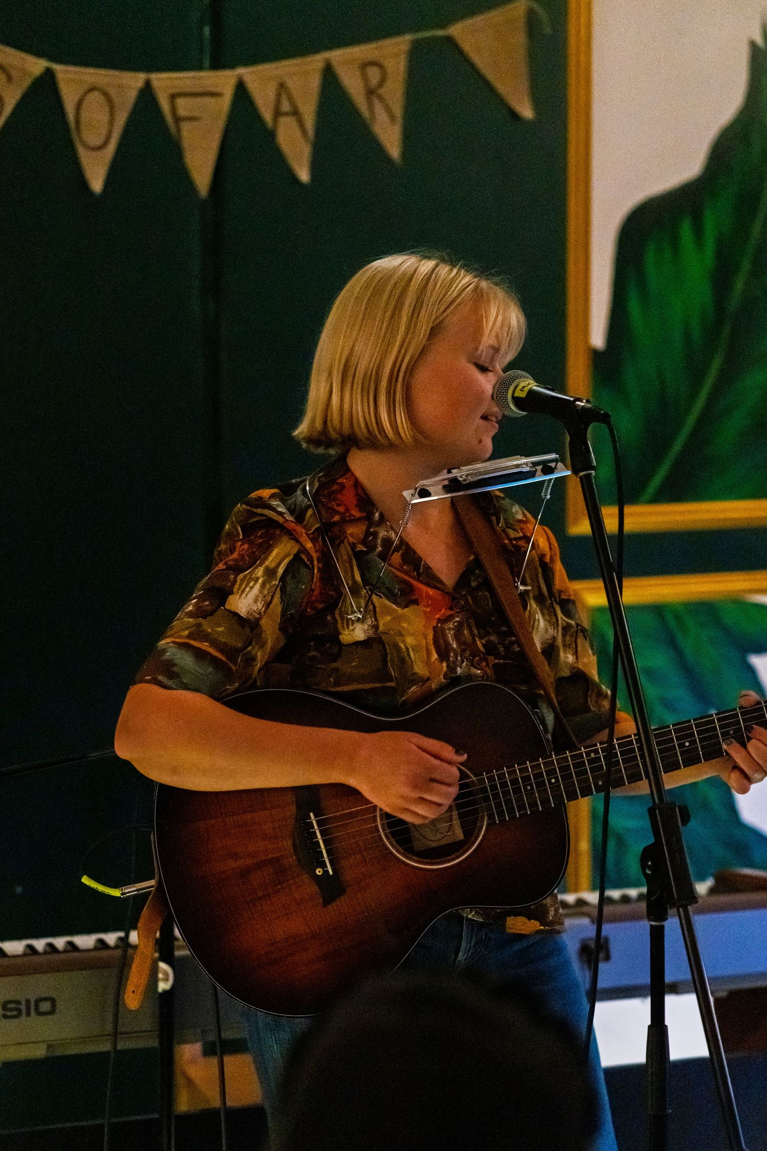 Musician performing with acoustic guitar under banner in intimate venue setting.