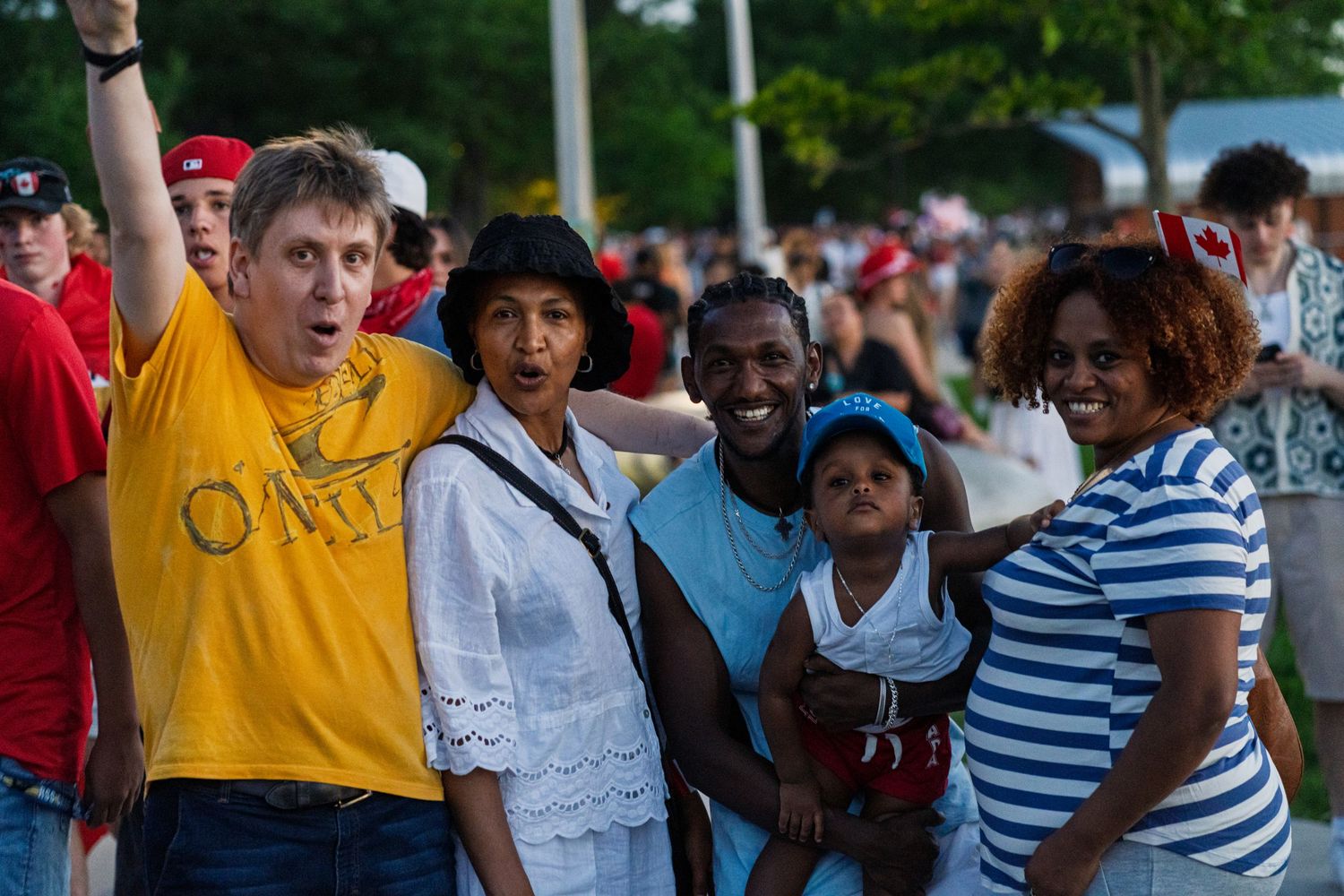 Diverse group of people at outdoor event with person in yellow shirt raising arm.