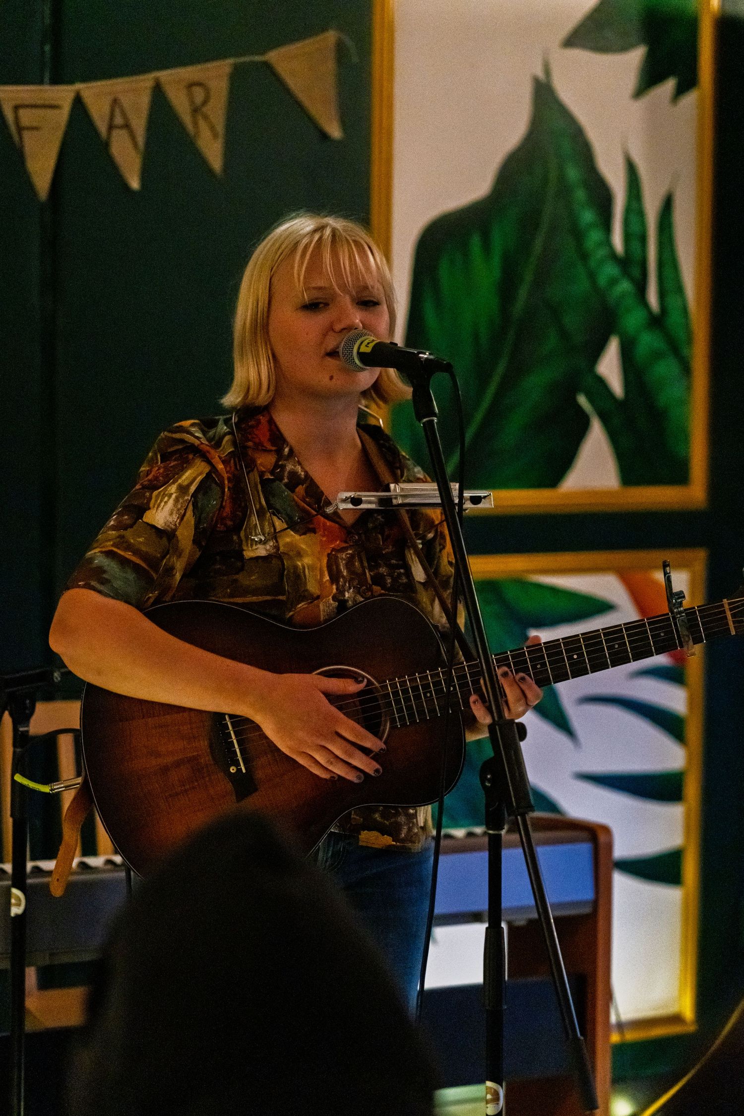 Musician performs with an acoustic guitar on stage under decorative bunting and lighting.