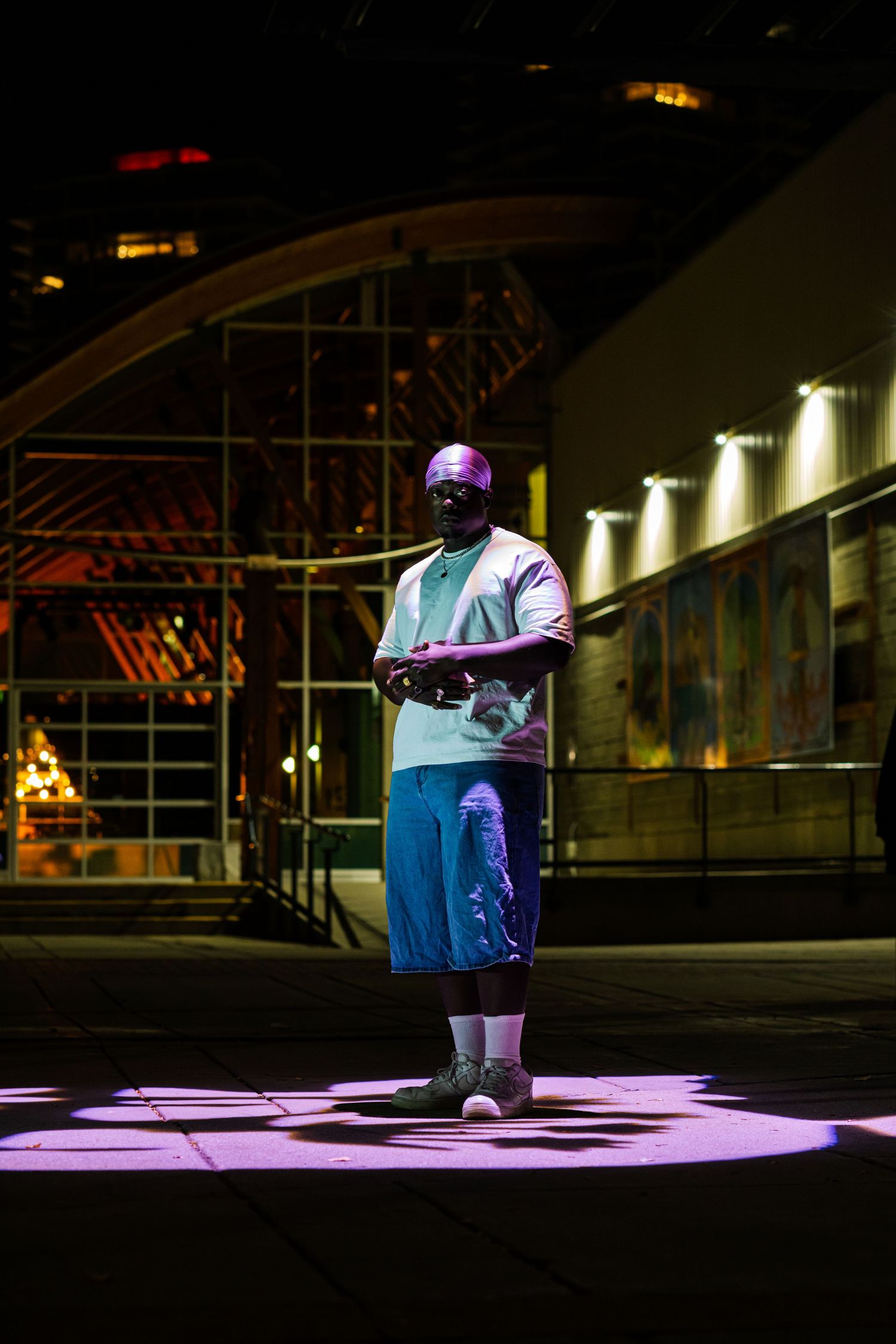 A person sits at a piano illuminated by dramatic purple and blue stage lighting in a dark performance space.