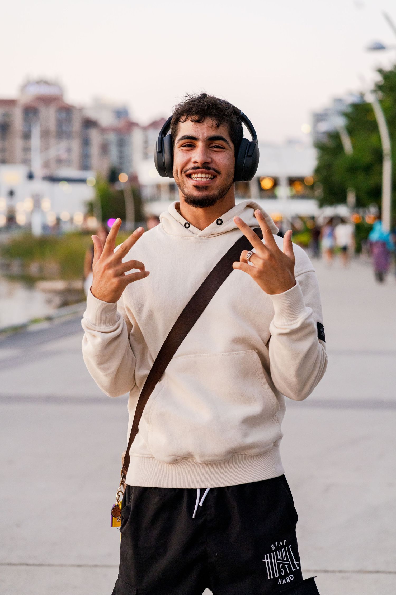Person in cream colored hoodie and dark pants making expressive gestures outdoors.